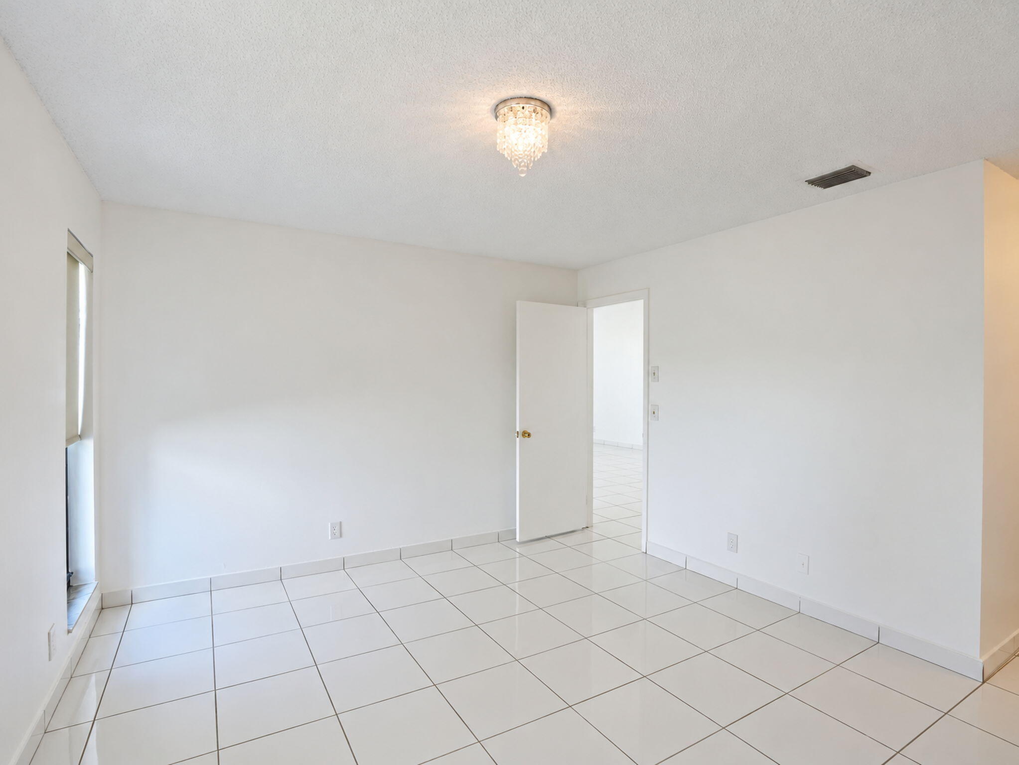 Interior space featuring polished white tile flooring, neutral wall finishes, and a decorative crystal flush-mount light fixture