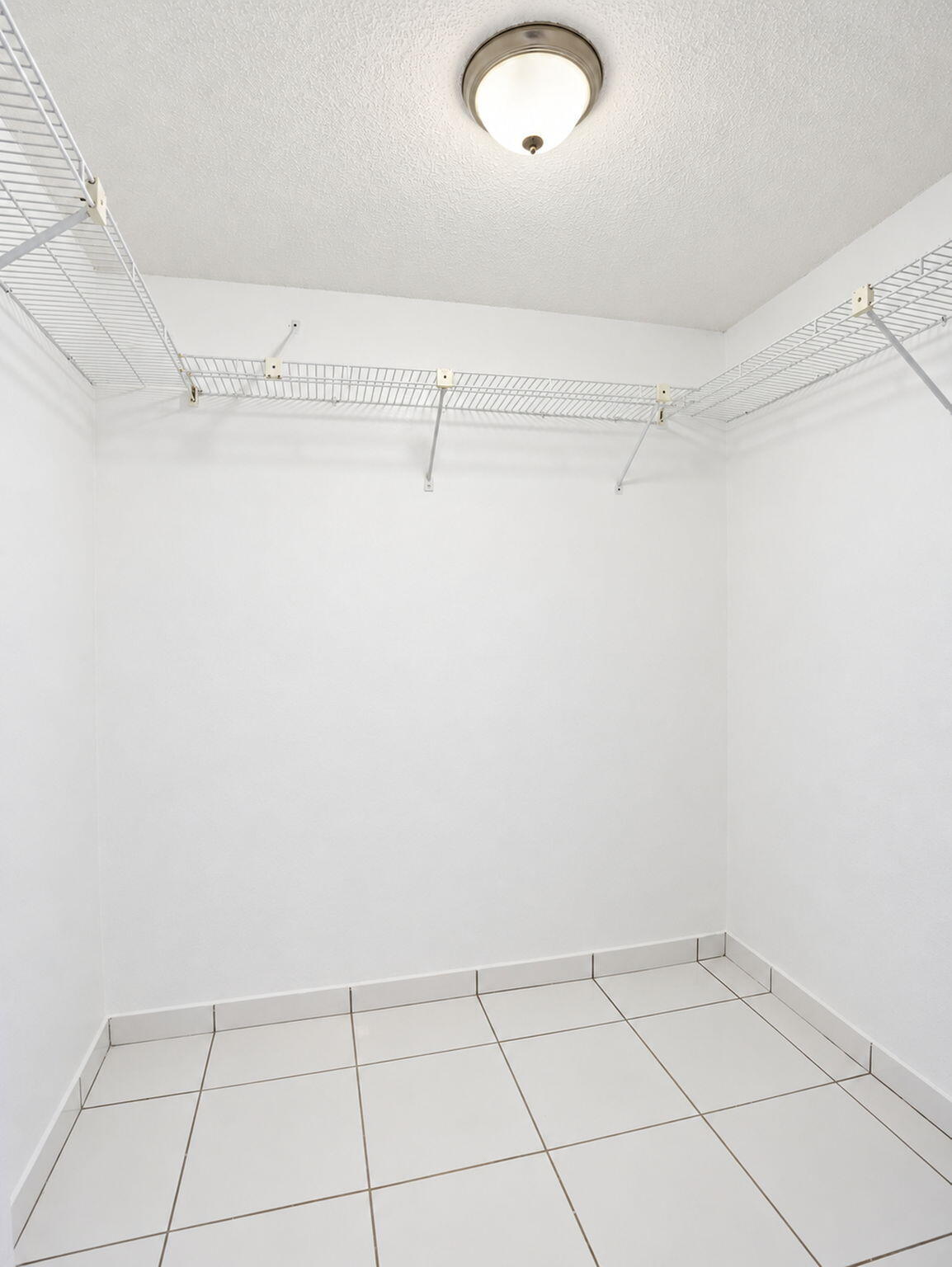 Storage area featuring white tile flooring, ceiling-mounted light fixture, and perimeter wire shelving