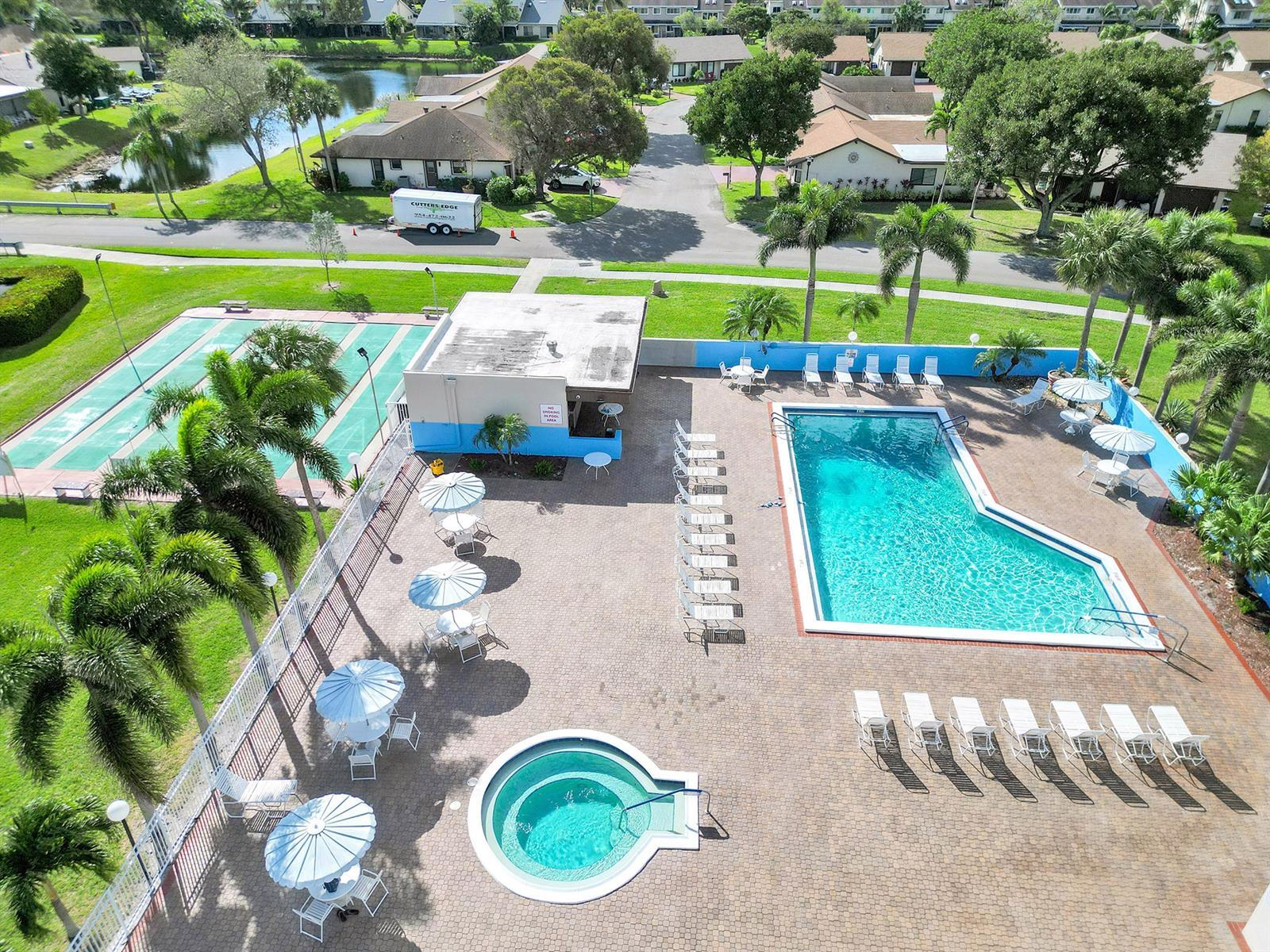 Community recreation area featuring a swimming pool, circular spa, paved deck, and adjacent shuffleboard courts