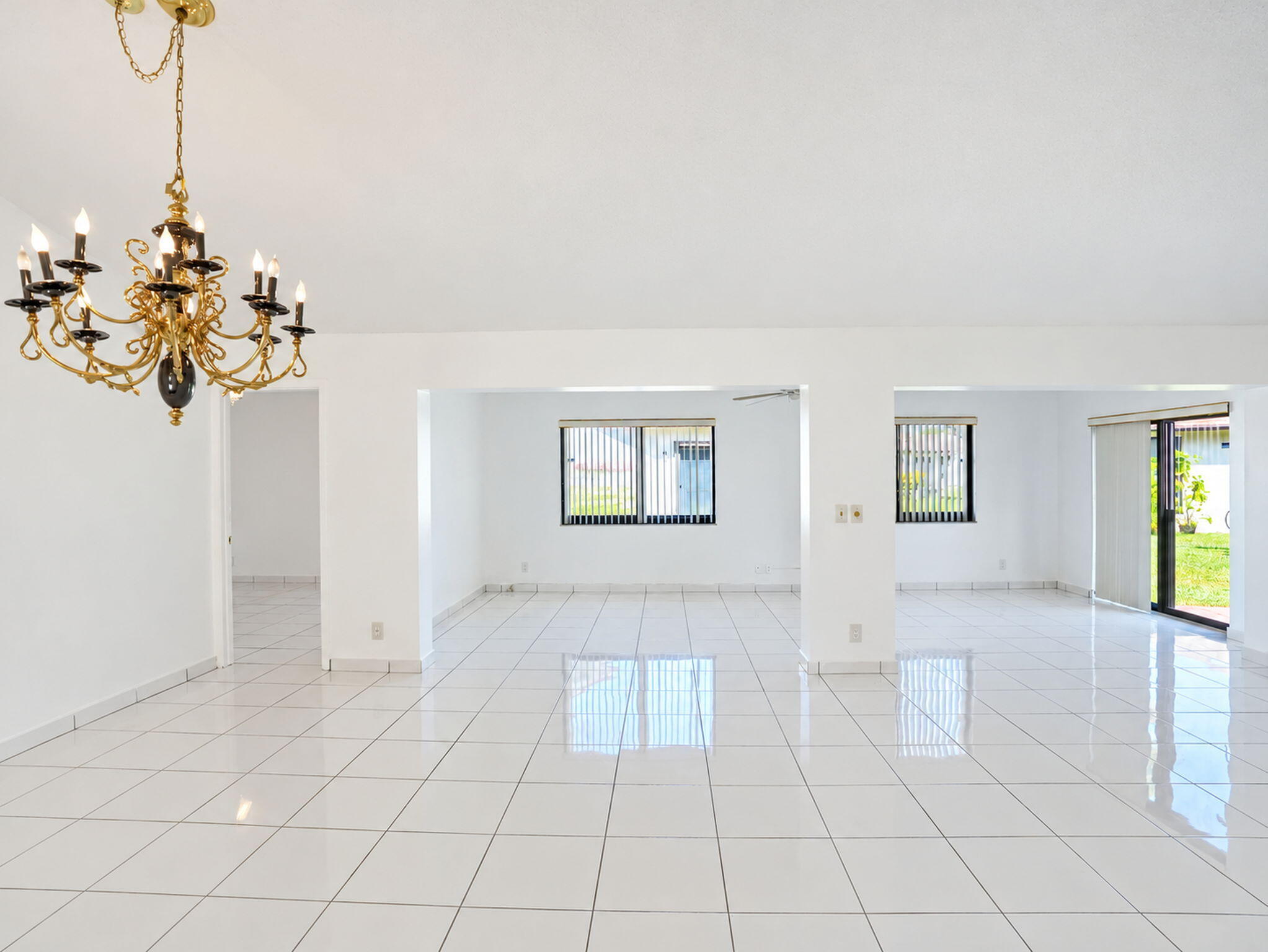 Open-concept interior featuring white tile flooring, gold-tone multi-arm chandelier, and sliding glass door