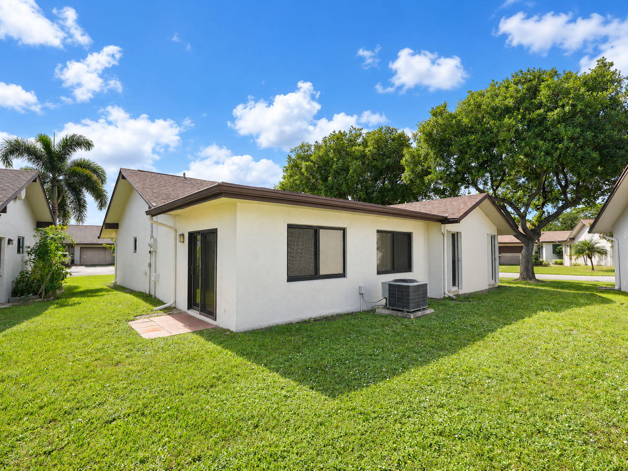 Stucco exterior featuring a gabled shingle roof, sliding glass doors, and expansive green space with mature trees