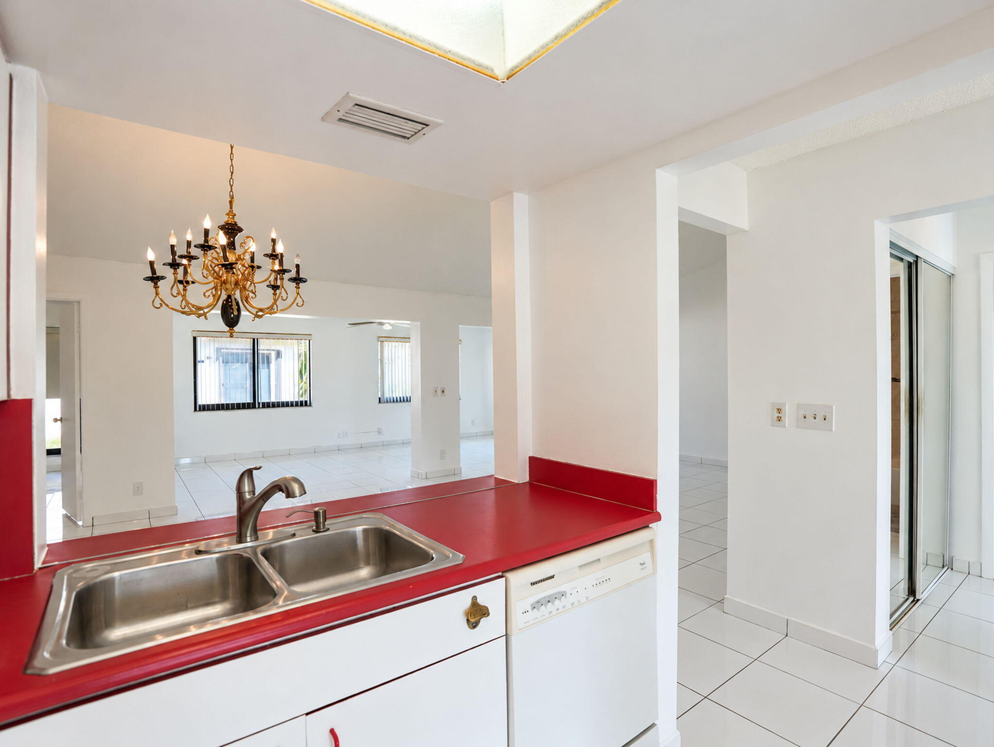 Kitchen featuring white cabinetry, solid-surface countertops, dual-basin stainless steel sink with high-arc faucet, integrated dishwasher, and overhead skylight