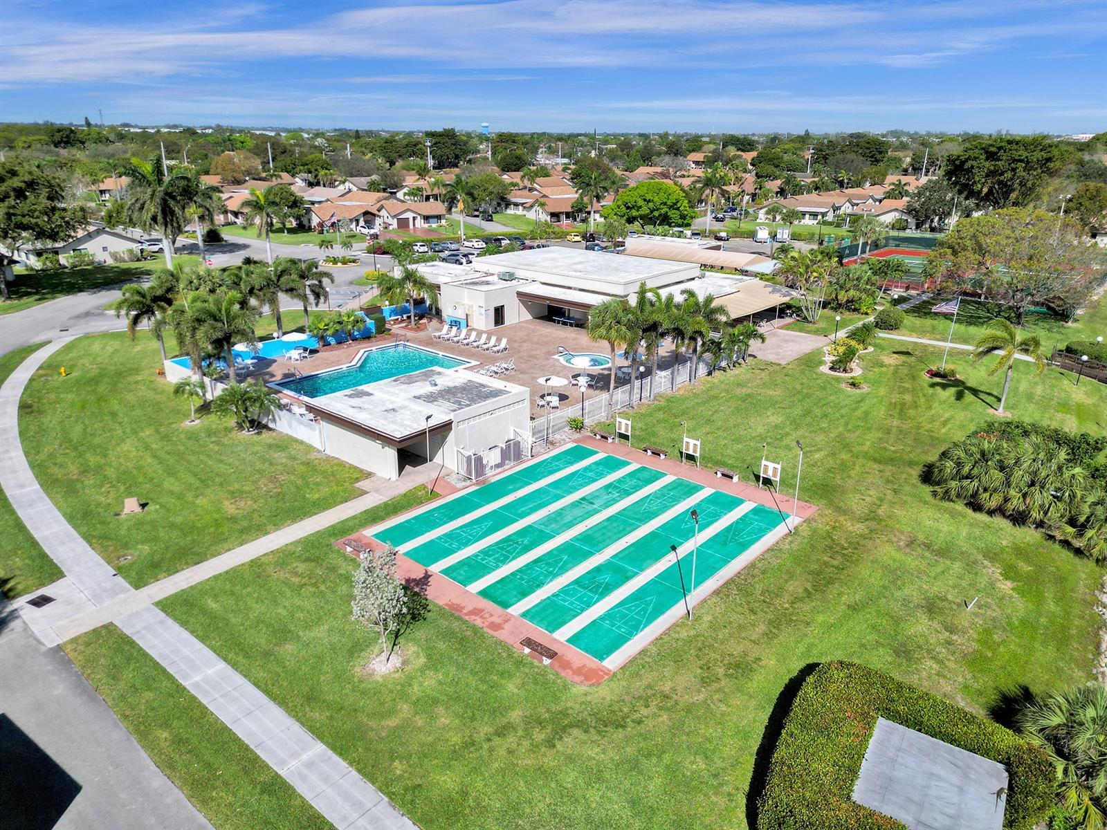 Community recreational area featuring a swimming pool, shuffleboard courts, tennis court, and a clubhouse with a paved patio