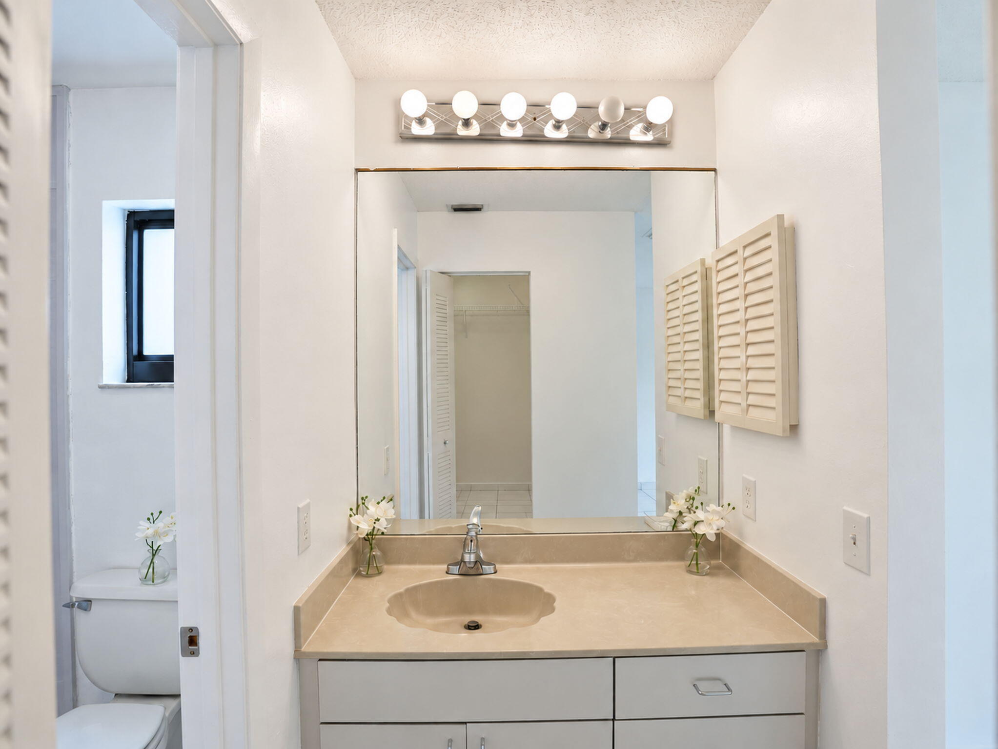 Bathroom vanity featuring a solid-surface countertop with an integrated scalloped basin, white cabinetry, a large frameless mirror, and a multi-bulb vanity light fixture