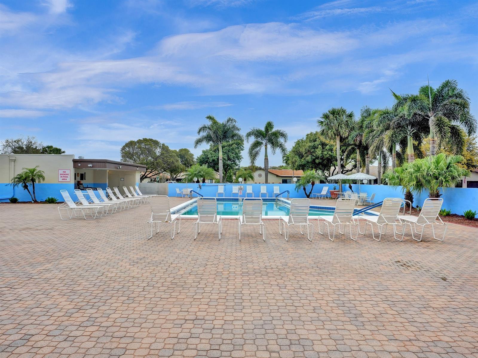 In-ground swimming pool featuring paver decking, perimeter privacy wall, and mature palm landscaping