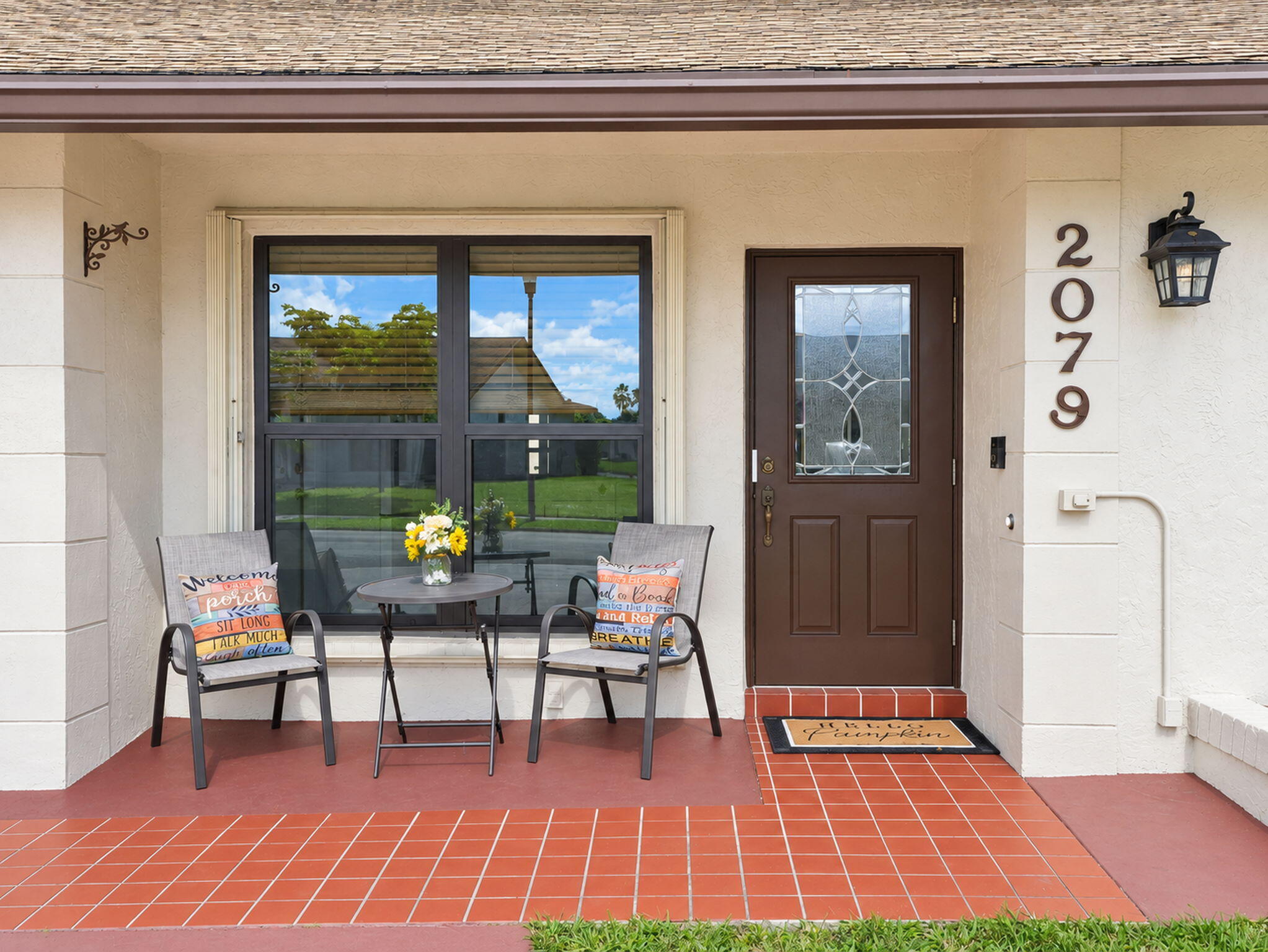 Stucco exterior entrance featuring a tile-paved porch, a solid door with an integrated glass inlay, and an attached traditional-style sconce
