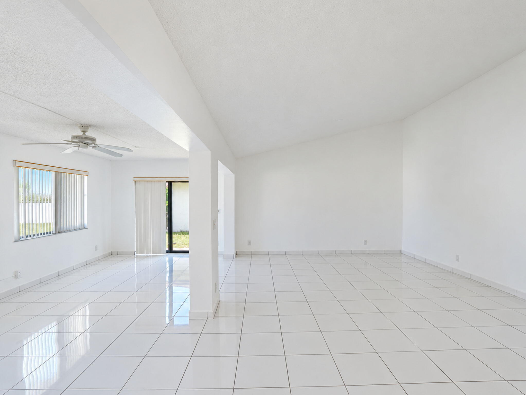 Open-concept interior featuring vaulted ceilings, polished tile flooring, a mounted ceiling fan, and sliding glass doors