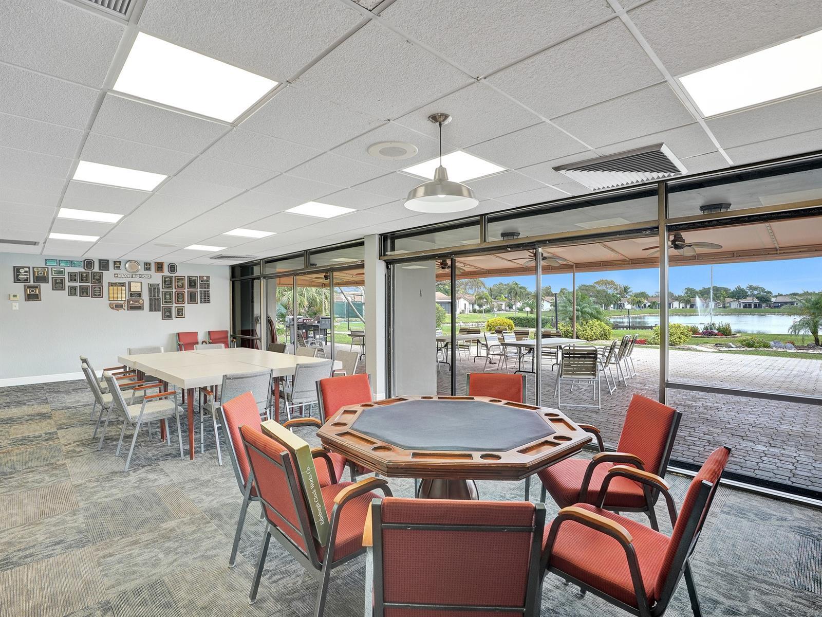 Multipurpose room featuring suspended ceiling tiles with integrated lighting, metal pendant lighting, expansive floor-to-ceiling glass sliding doors, and direct access to an outdoor paved patio