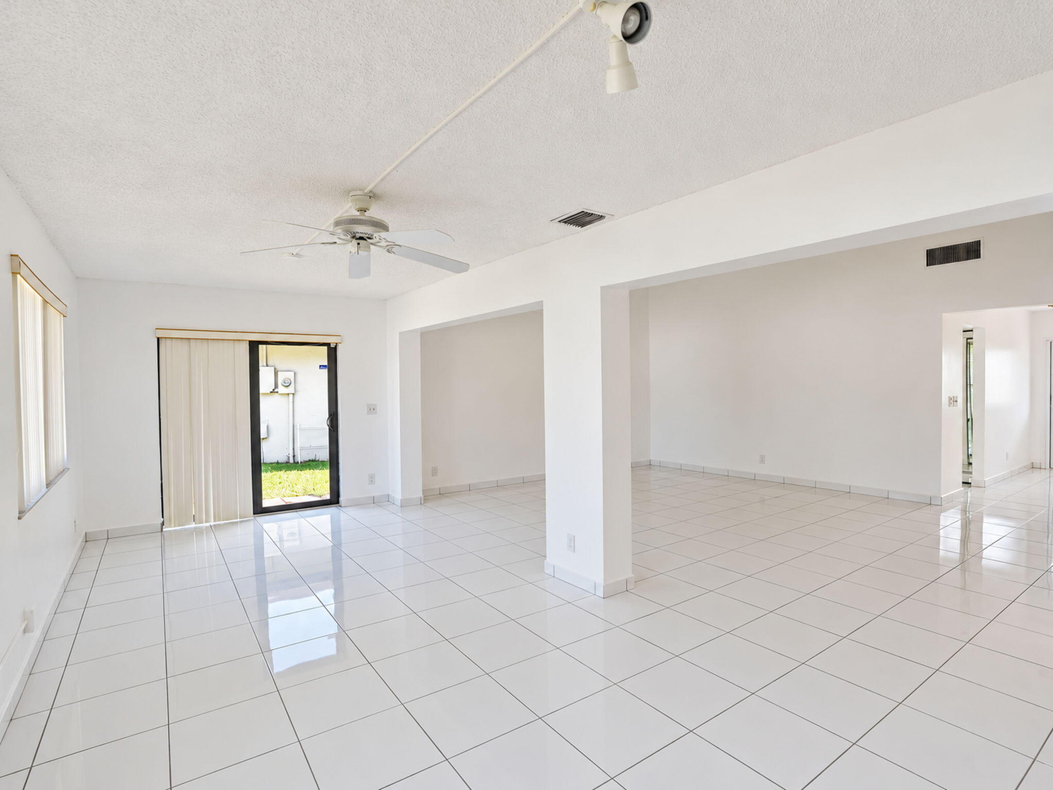 Open interior space featuring high-gloss ceramic tile flooring, a ceiling fan with integrated lighting, and glass sliding doors providing exterior access