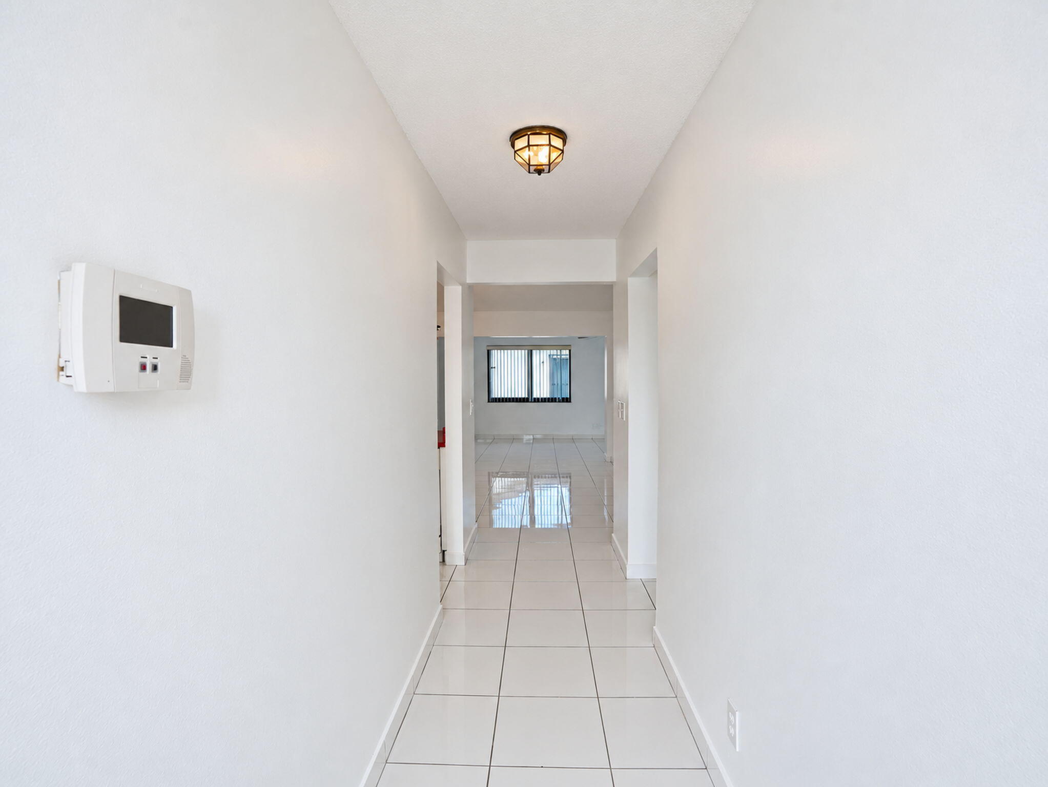 Hallway featuring neutral-toned tile flooring, flush-mount lighting, and a wall-mounted programmable thermostat