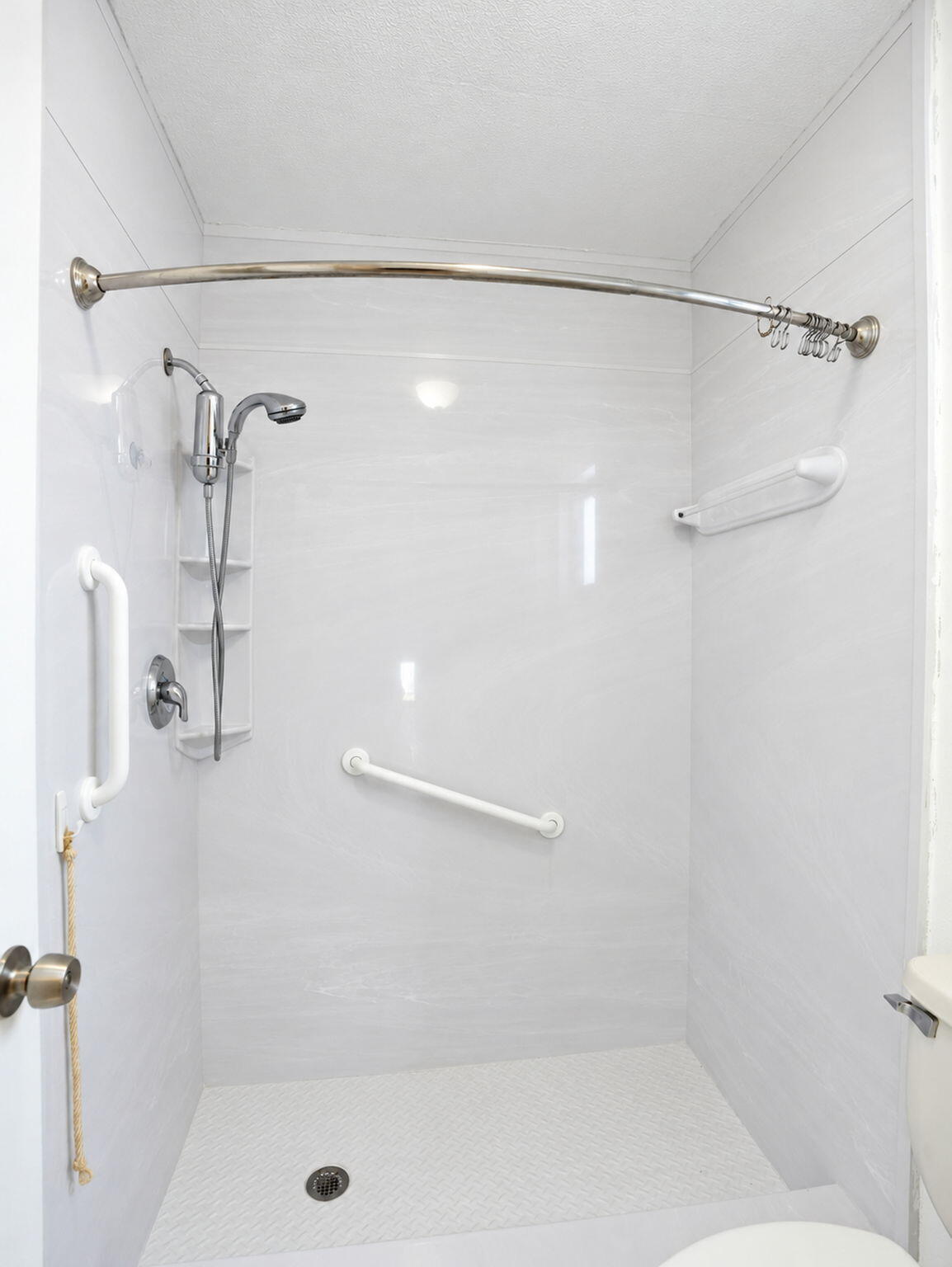Walk-in shower enclosure featuring white wall panels, a handheld shower fixture, a curved shower rod, and integrated support bars