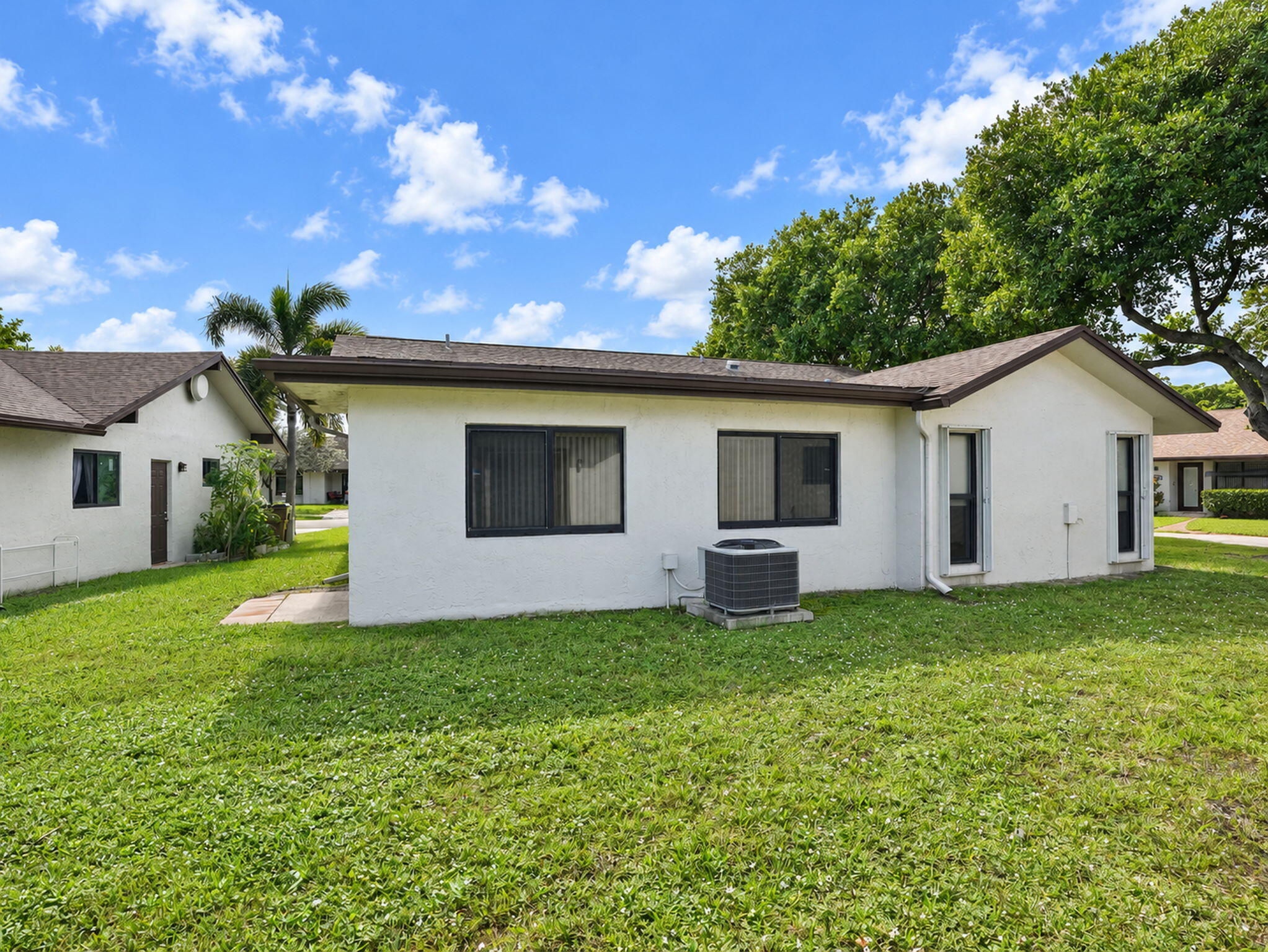 Stucco exterior with a low-pitch hip roof, dark-trimmed window frames, and expansive lawn area
