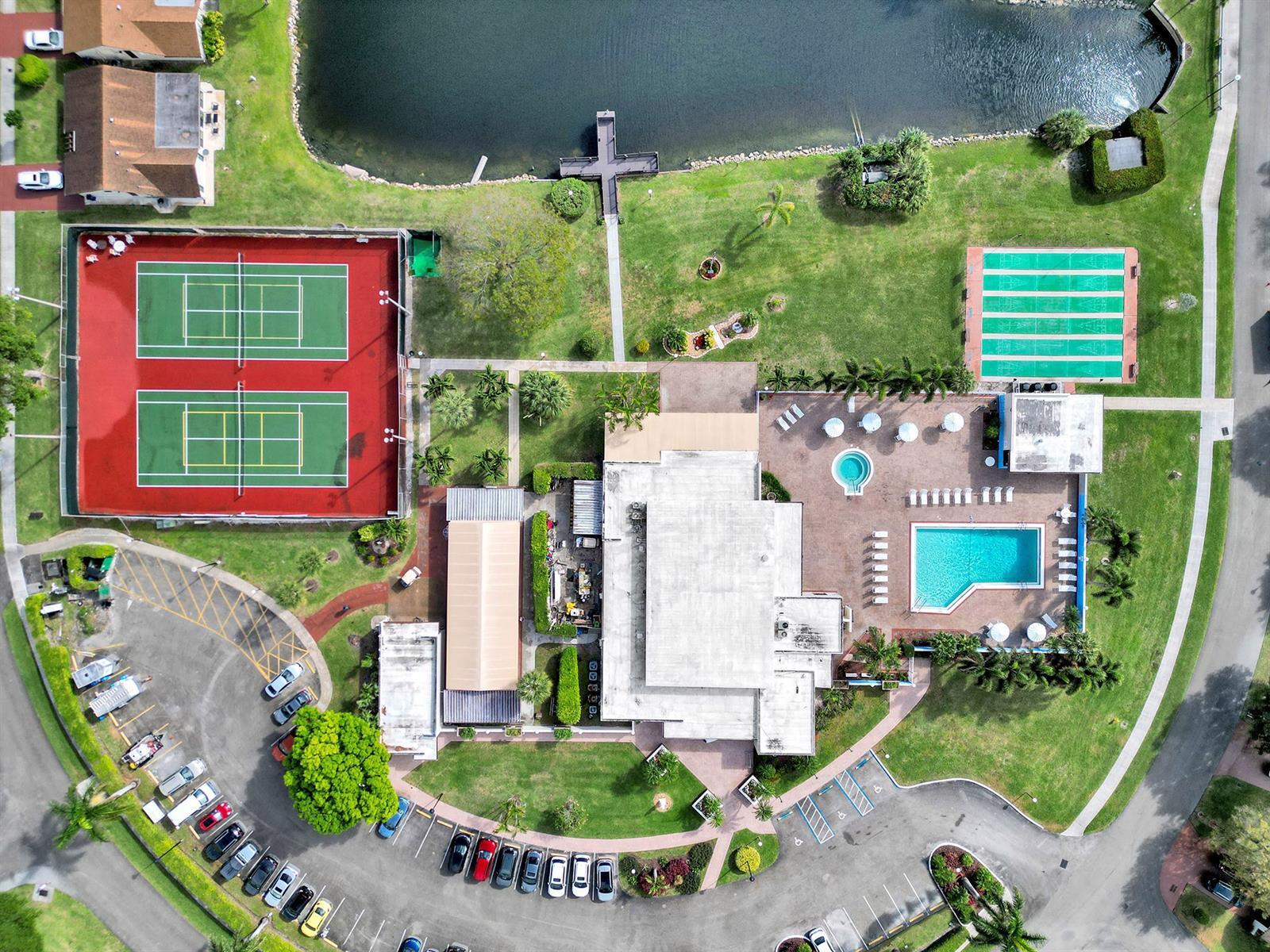 Aerial perspective featuring tennis courts, a swimming pool, a spa, a boat dock, and paved surface parking