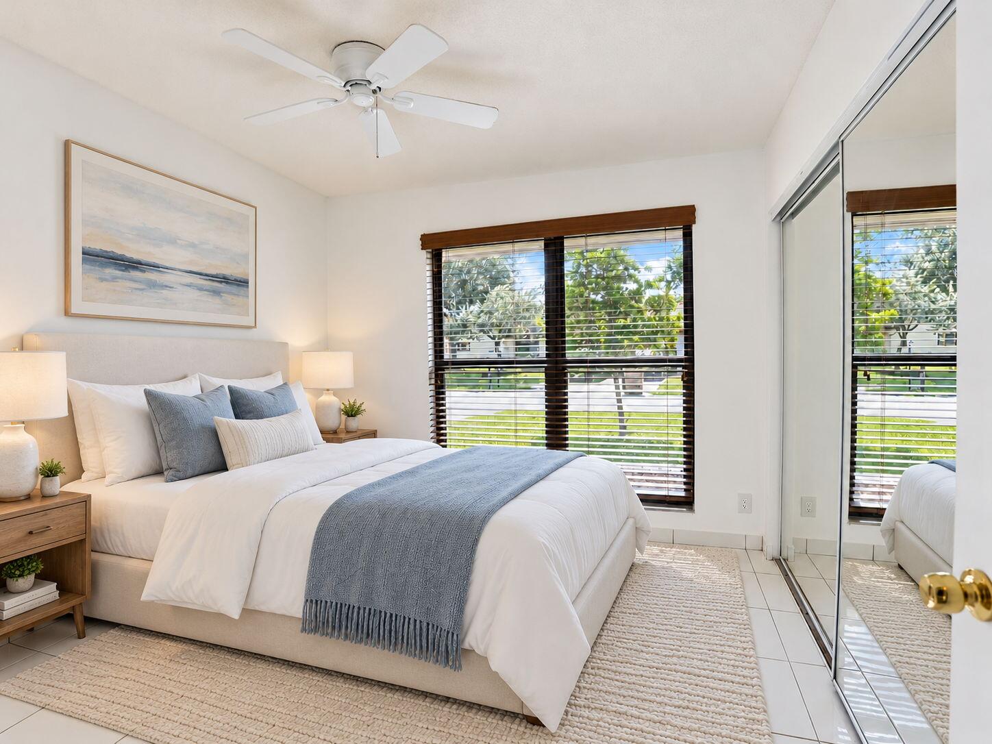 Bedroom featuring neutral tile flooring, a white ceiling fan, large windows with horizontal blinds, and a built-in closet with mirrored sliding doors