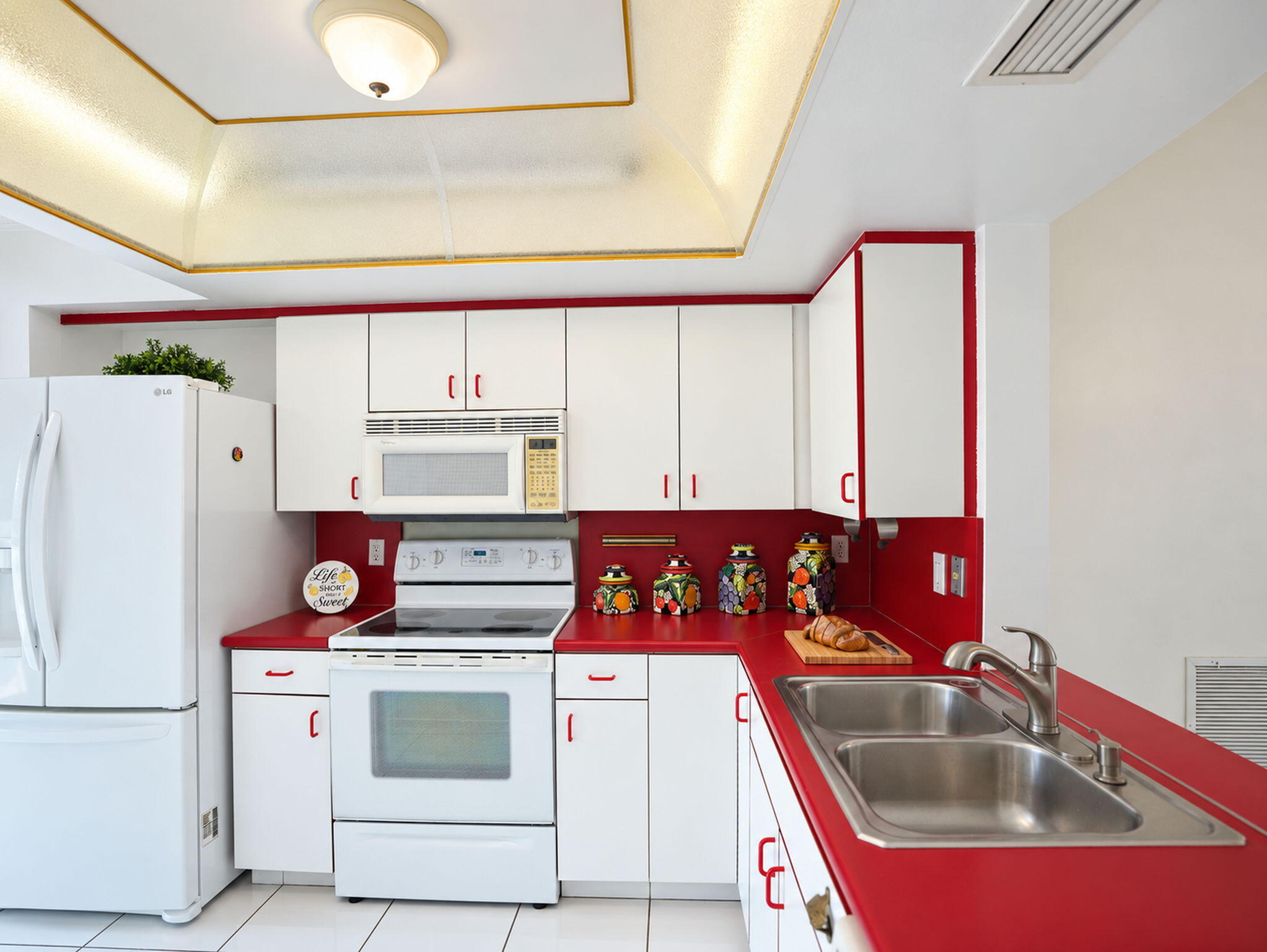 Kitchen featuring white cabinetry, solid-surface countertops, dual-basin stainless steel sink with pull-down faucet, recessed tray ceiling, and tile flooring