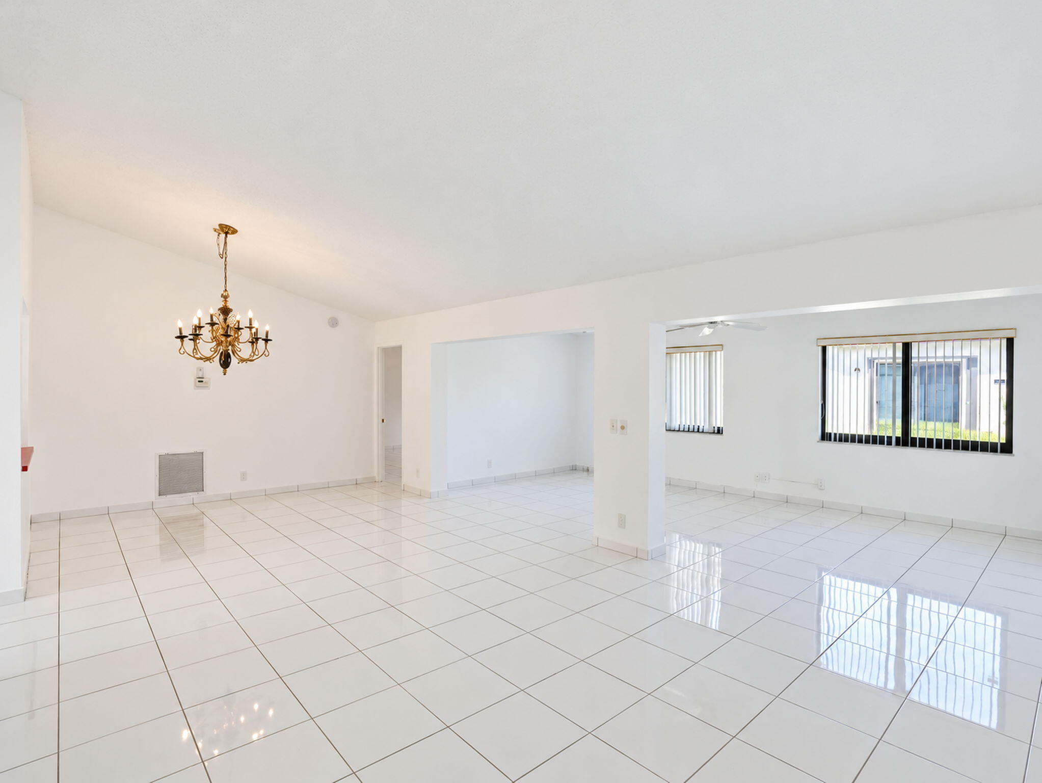 Open-concept interior featuring vaulted ceilings, polished tile flooring, a multi-arm metallic chandelier, and horizontal window blinds