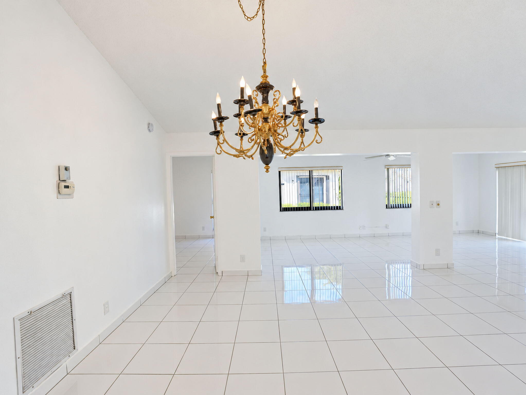 Open interior space featuring vaulted ceilings, polished ceramic tile flooring, a multi-tiered gold-tone chandelier, and large windows with horizontal blinds