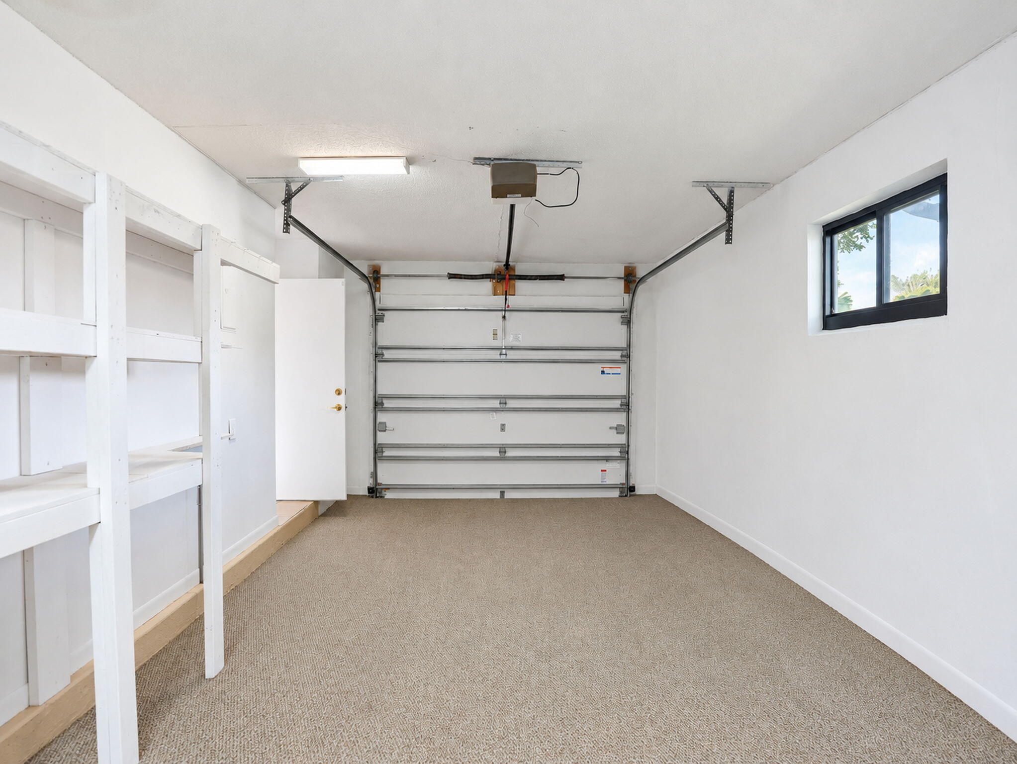 Finished garage featuring white walls, textured flooring, built-in shelving, an automatic overhead door, and a single-pane window