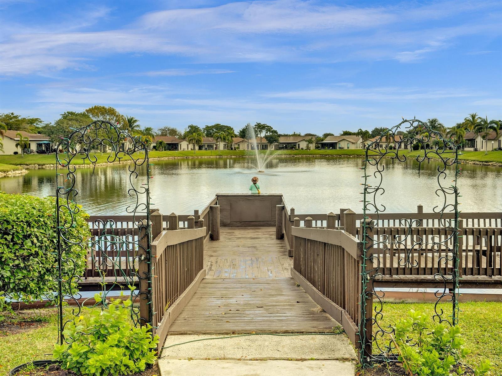 Waterfront wooden pier featuring a decorative metal archway, integrated railings, and a water fountain
