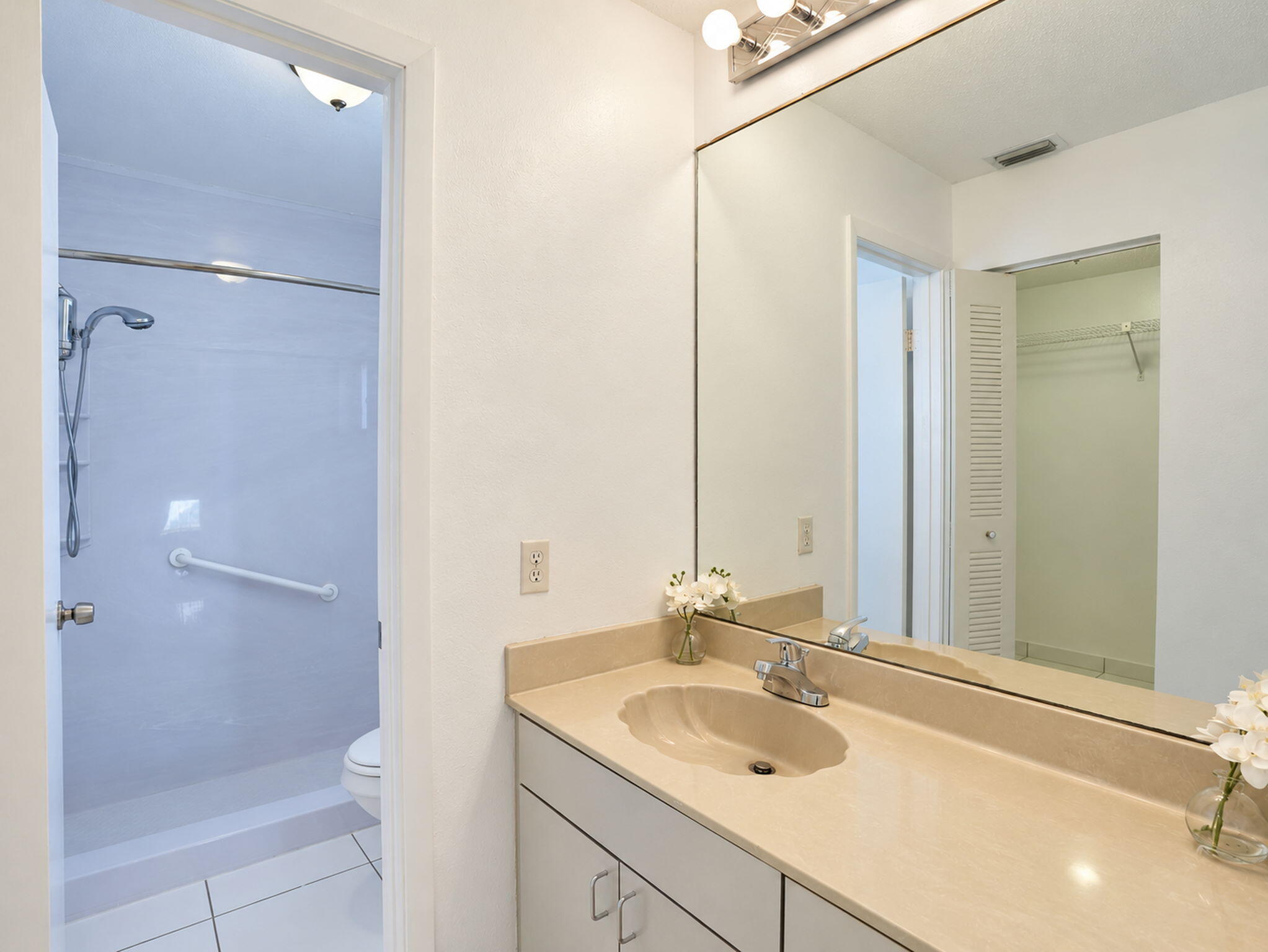 Bathroom featuring a solid-surface vanity countertop with an integrated scalloped sink, large-format wall mirror, chrome plumbing fixtures, and white cabinetry