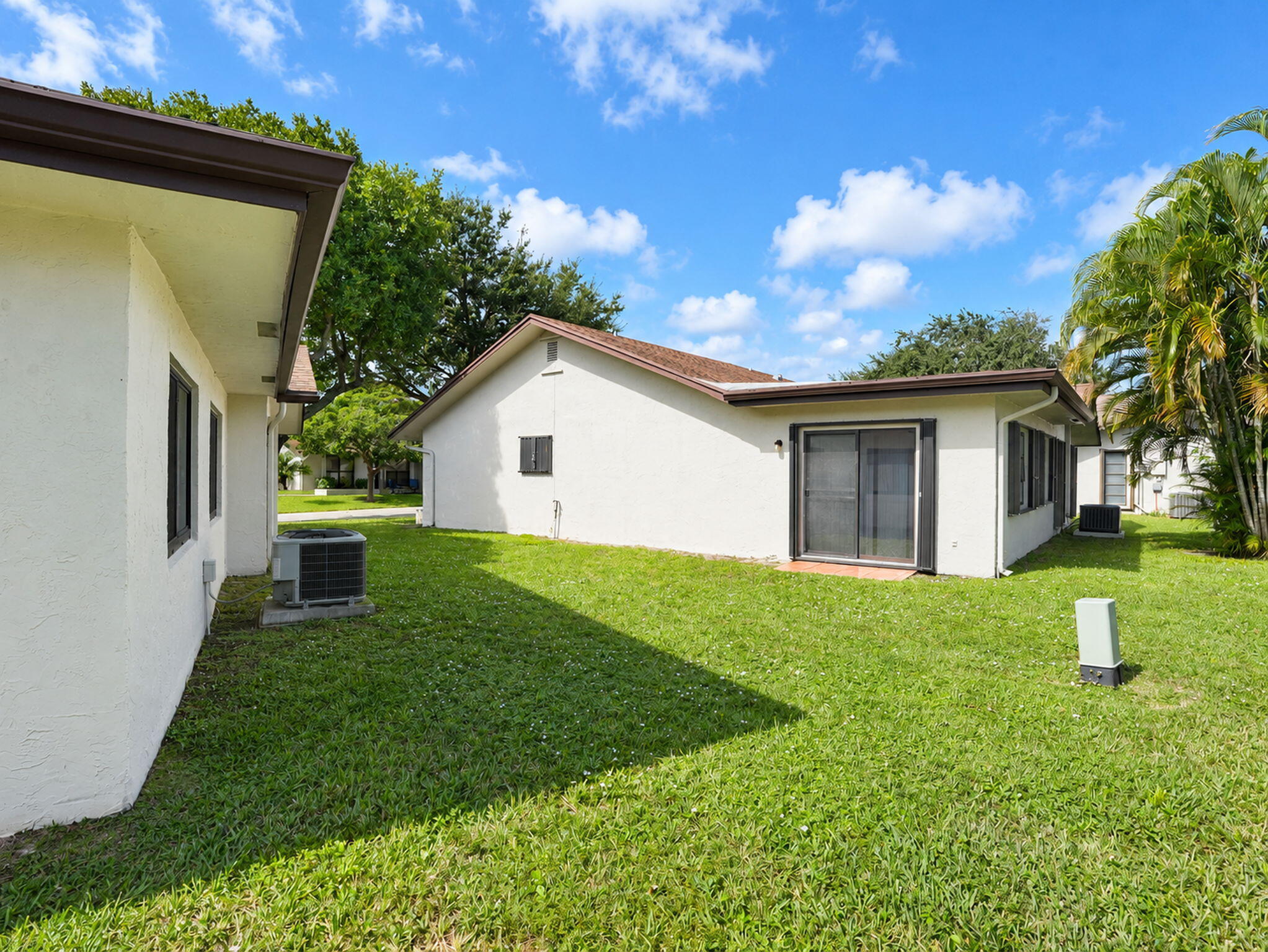 Stucco exterior with sliding glass doors, shingle roofing, and expansive lawn area