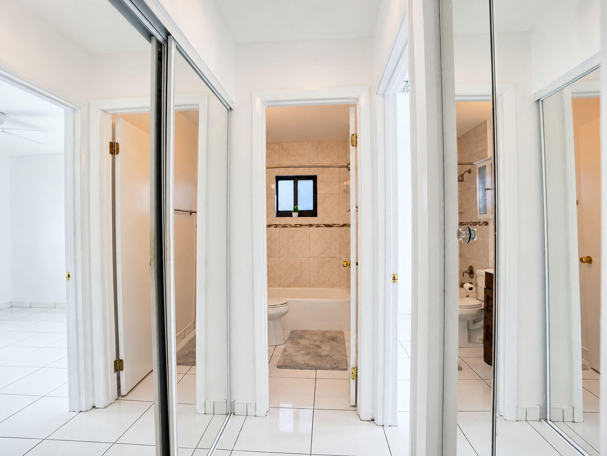Ceramic tile flooring, sliding mirrored closet doors, and interior doorway with access to a bathroom featuring stone-finish wall tile and a built-in bathtub