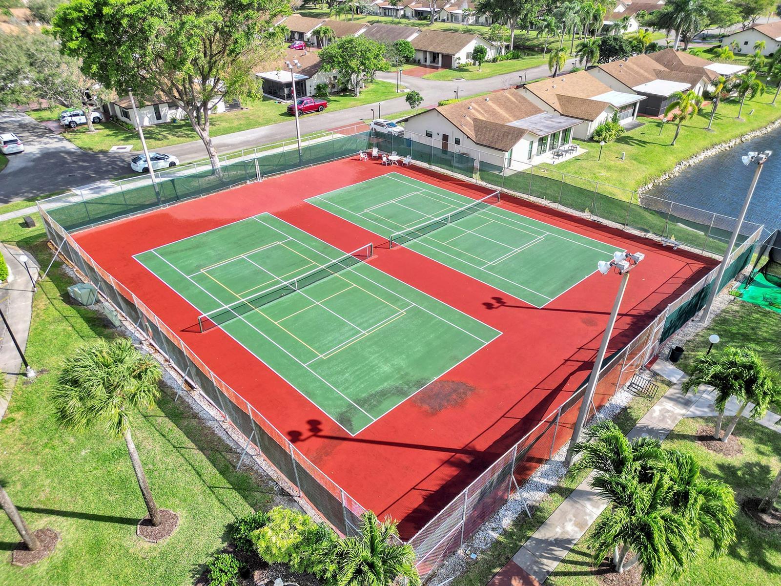 Dual tennis courts featuring high-visibility fencing, overhead lighting systems, and perimeter landscaping