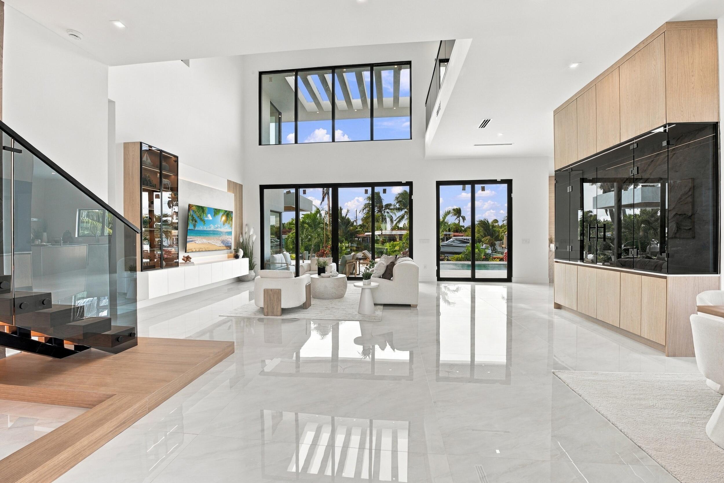 Double-height living area featuring floor-to-ceiling glass doors, large-format tile flooring, a custom staircase with glass railing, and built-in floor-to-ceiling cabinetry