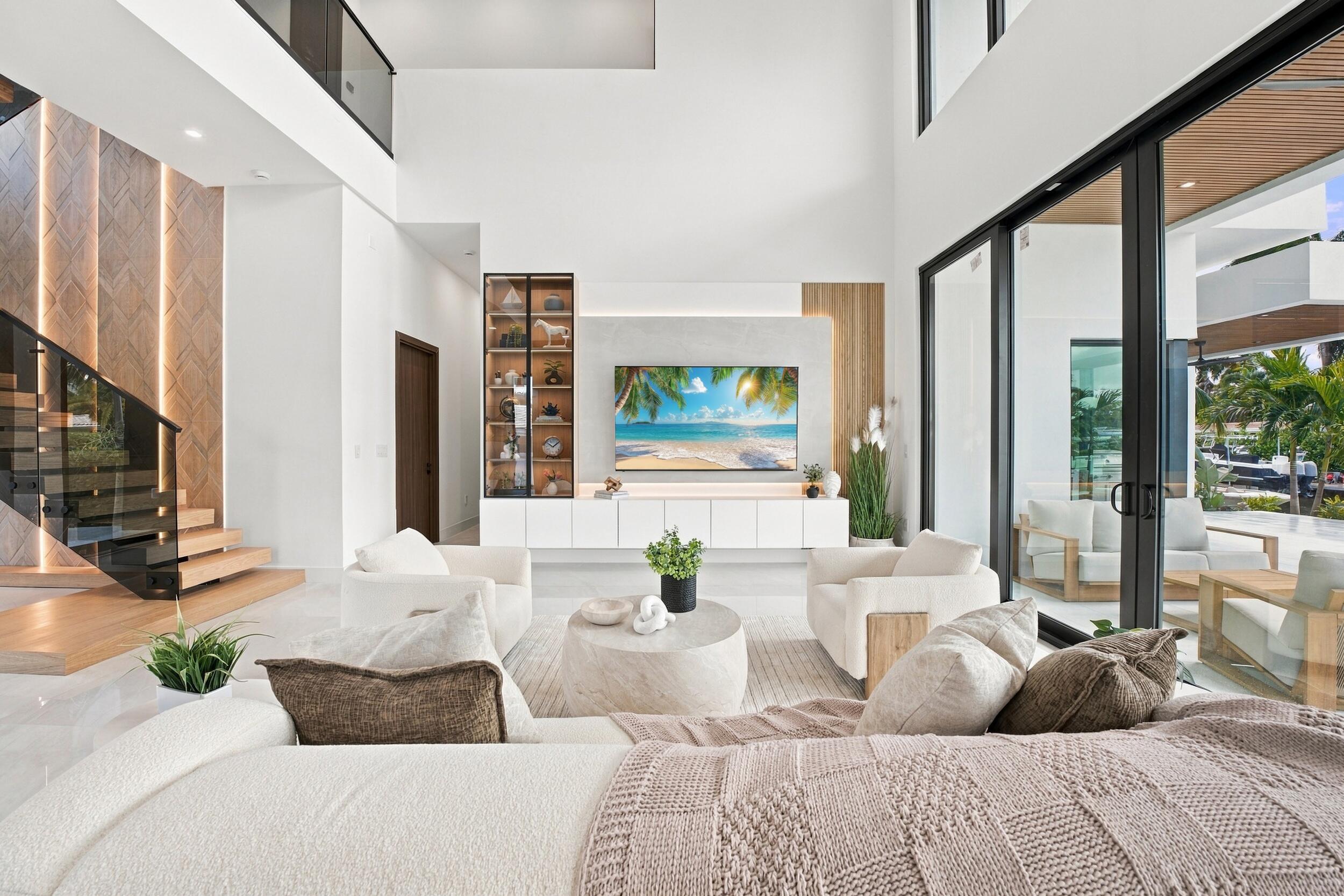 Double-height ceilings, floating staircase with integrated vertical lighting, floor-to-ceiling glass panel doors, and custom built-in cabinetry featuring wood accents and display shelving