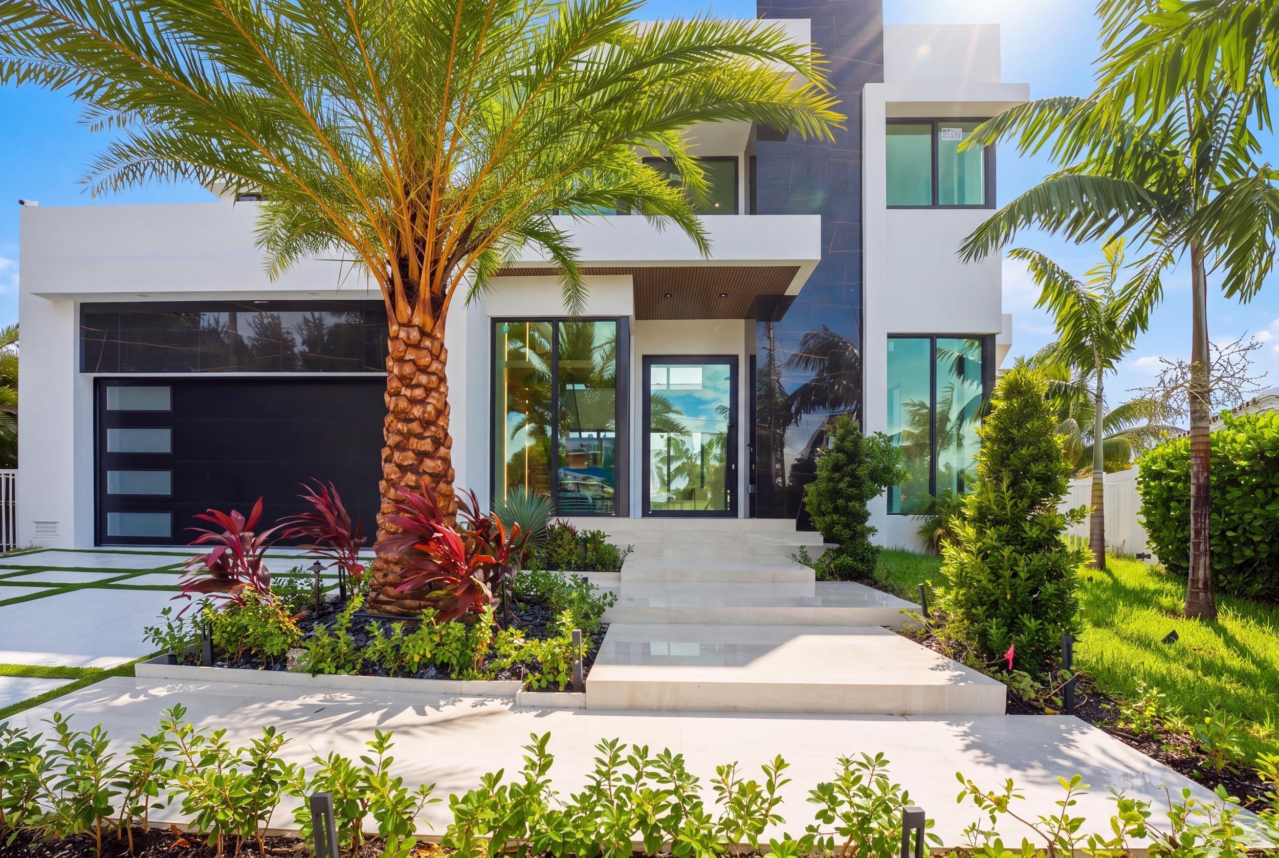 Modern architectural exterior featuring smooth white stucco finish, high-contrast dark stone accents, expansive floor-to-ceiling windows, integrated garage door with horizontal glass panels, and manicured landscaping