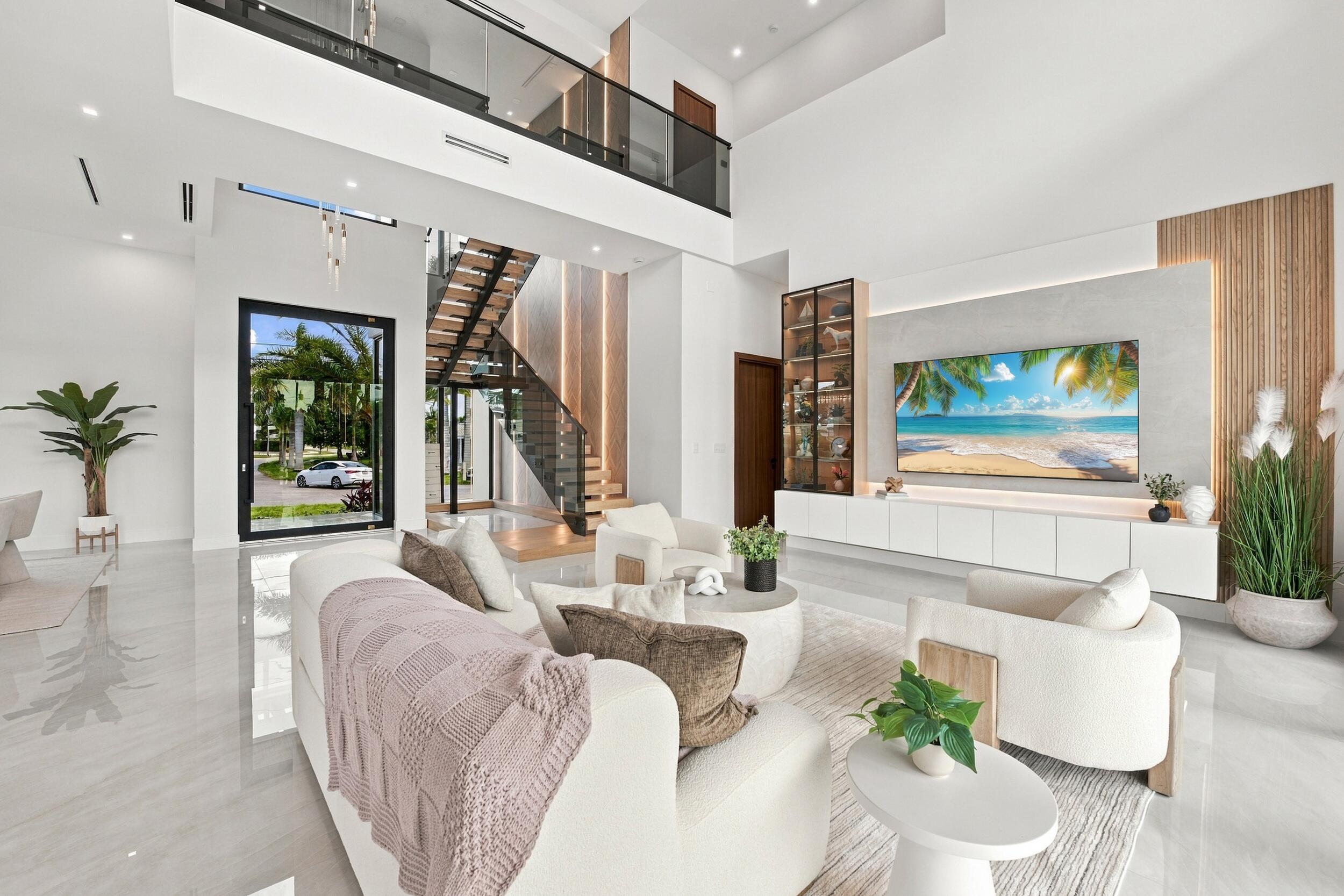 Double-height living area featuring floor-to-ceiling windows, porcelain flooring, a floating media console with integrated shelving, and an open-riser staircase with a glass railing