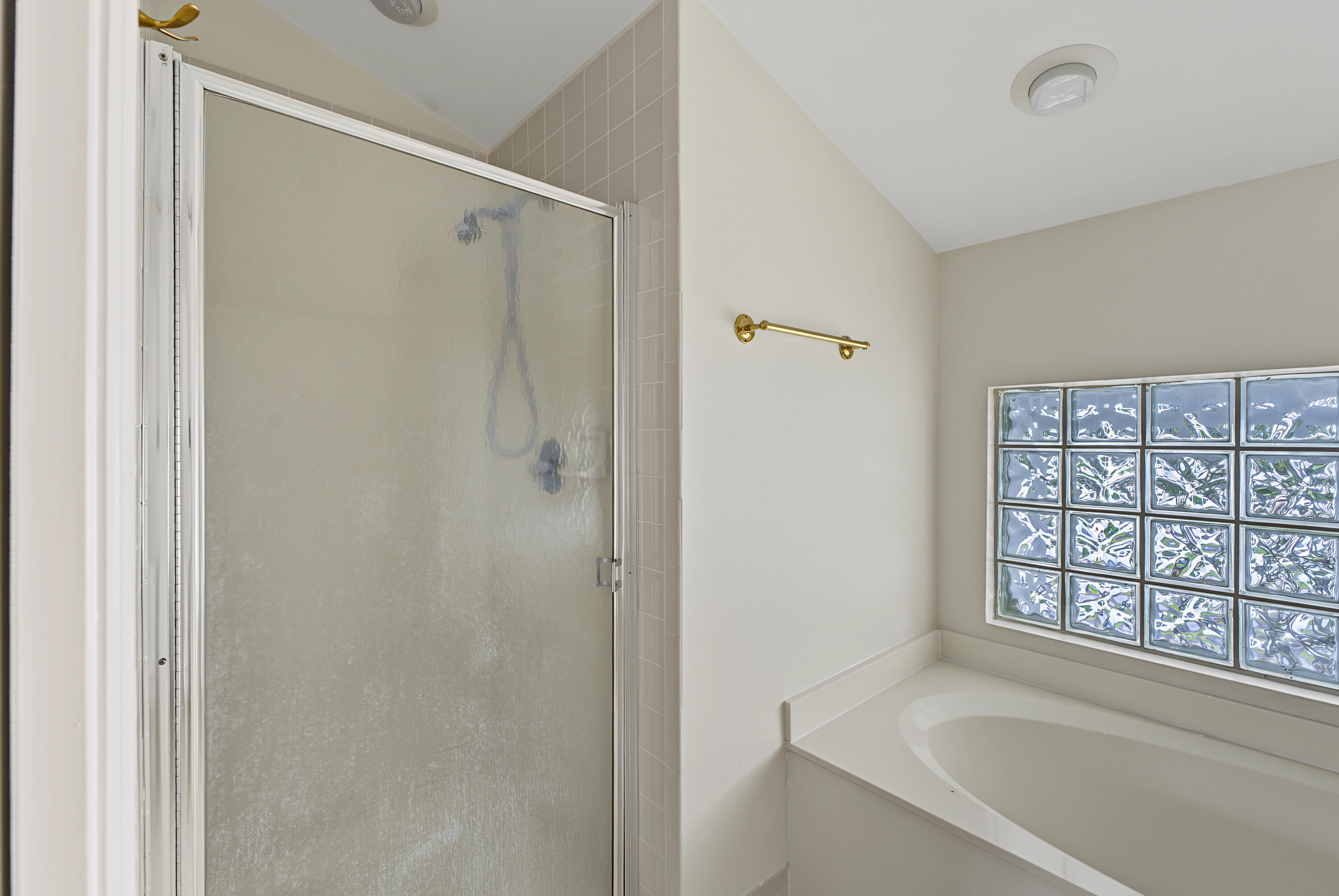Shower with a glass enclosure, soaking tub, and glass block window