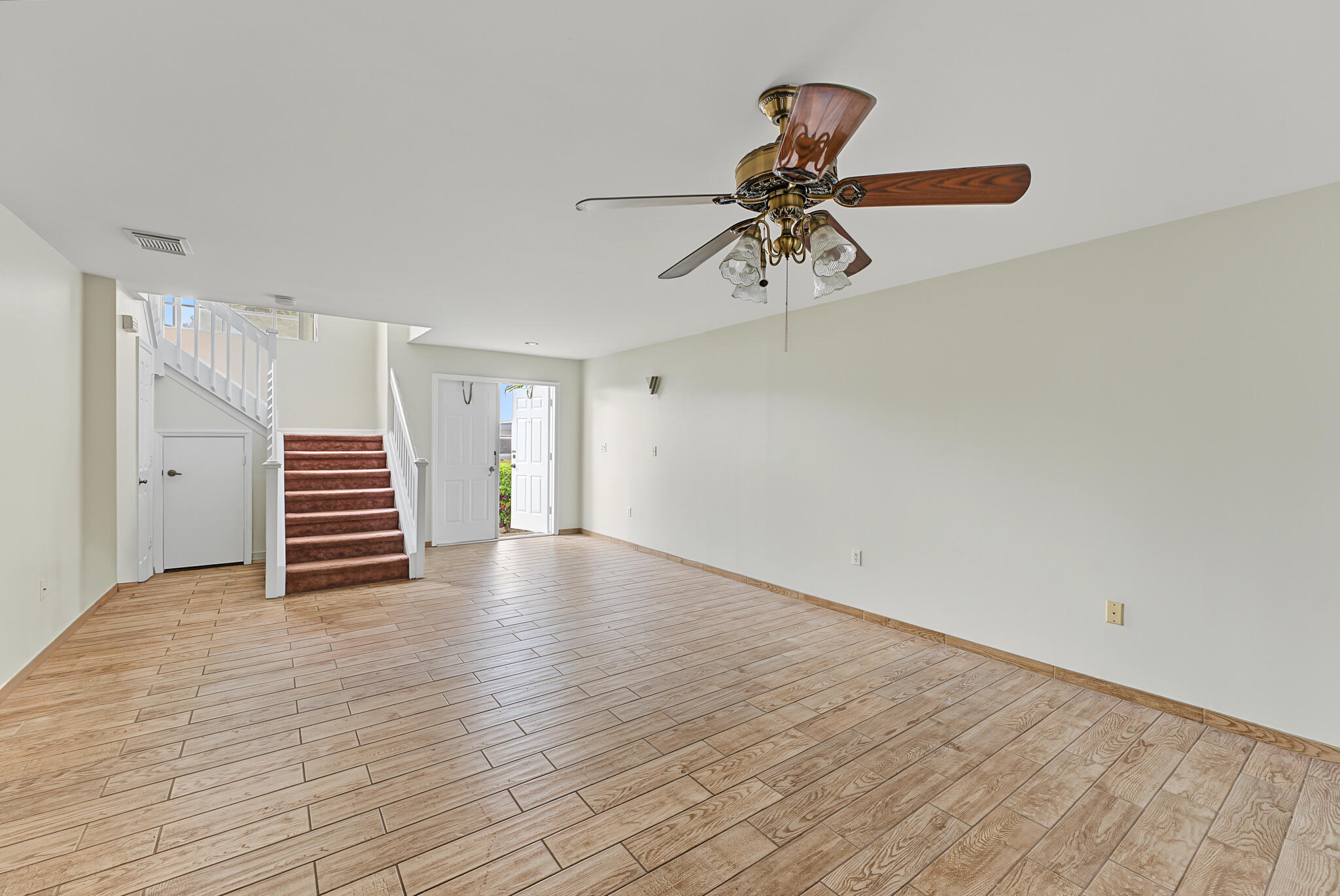 Open-concept interior featuring wood-finish tile flooring, a ceiling fan with multi-light fixture, and a staircase with white balusters