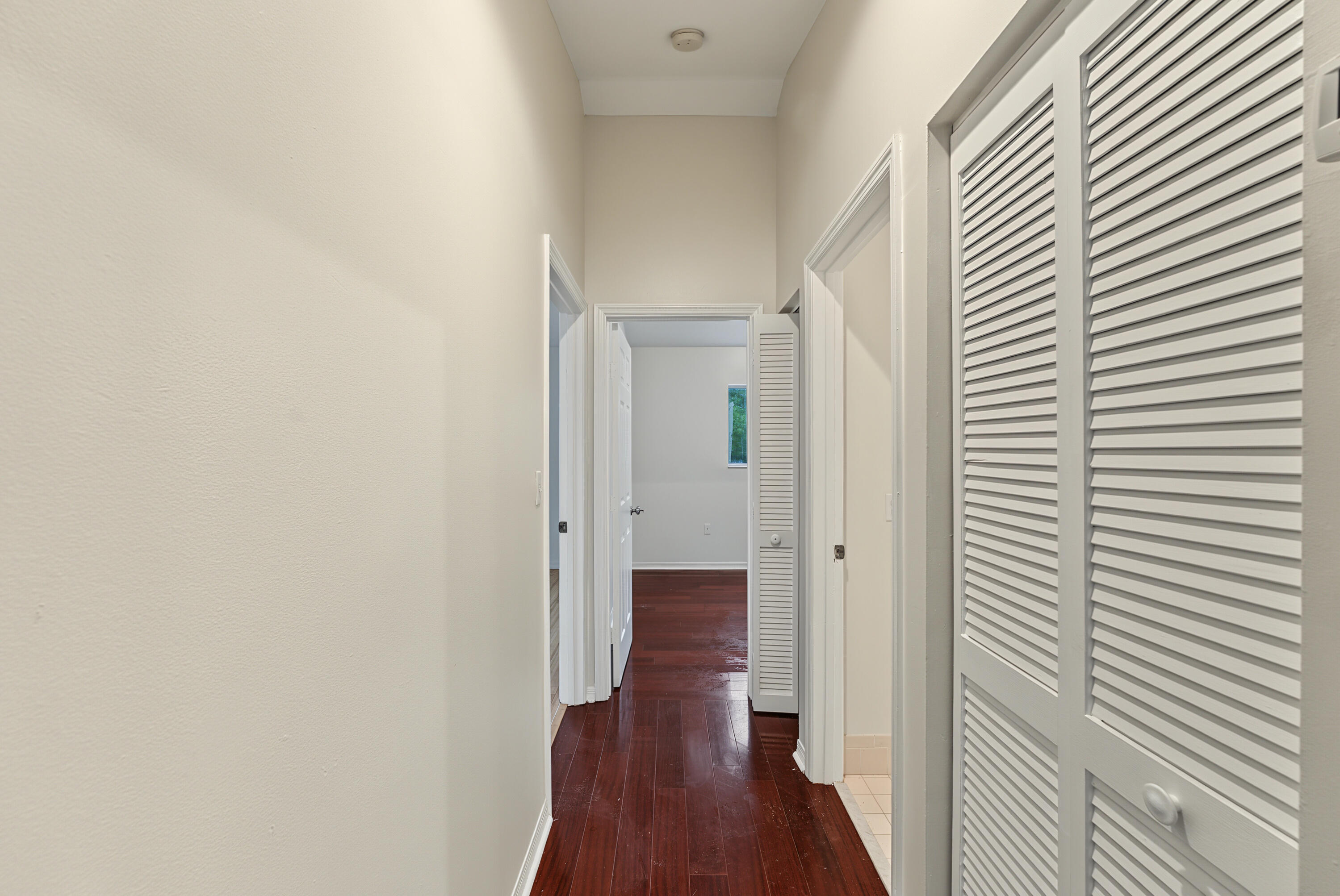 Hallway featuring high ceilings, wood-finish flooring, and white louvered closet doors