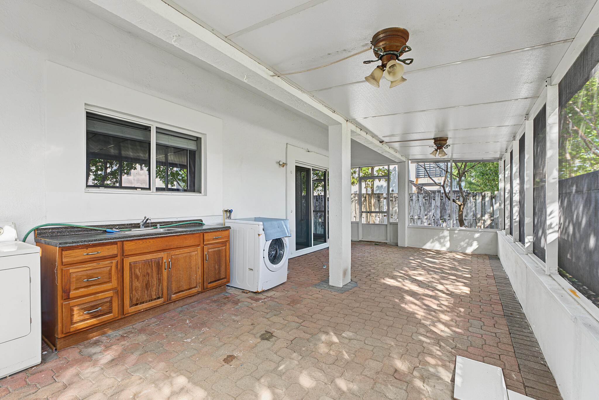 Covered screened-in patio featuring brick paver flooring, built-in wooden cabinetry with a sink, dual ceiling fans, and sliding glass entry doors