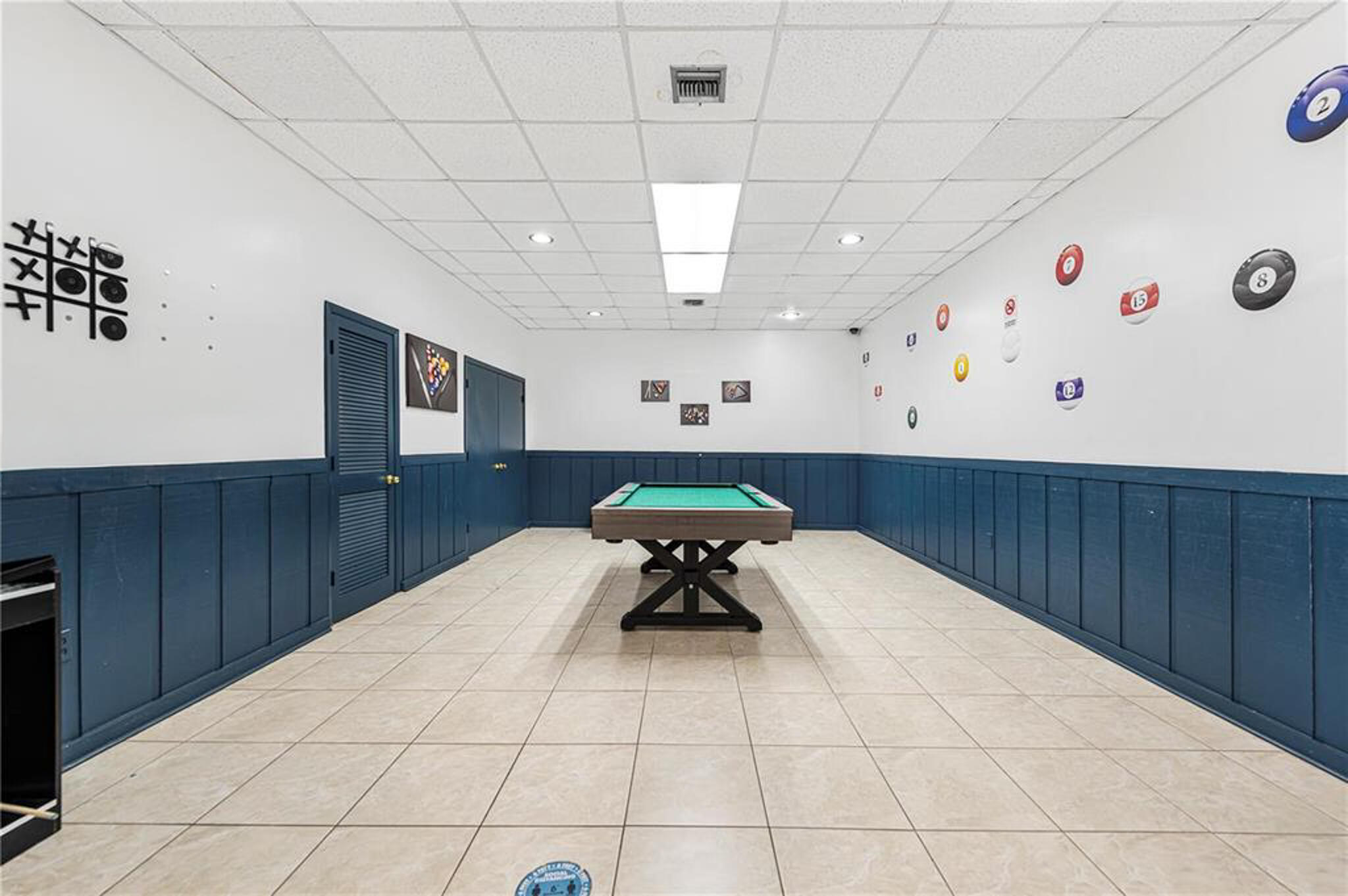 Room featuring ceramic tile flooring, blue board-and-batten wainscoting, and a drop ceiling with recessed lighting