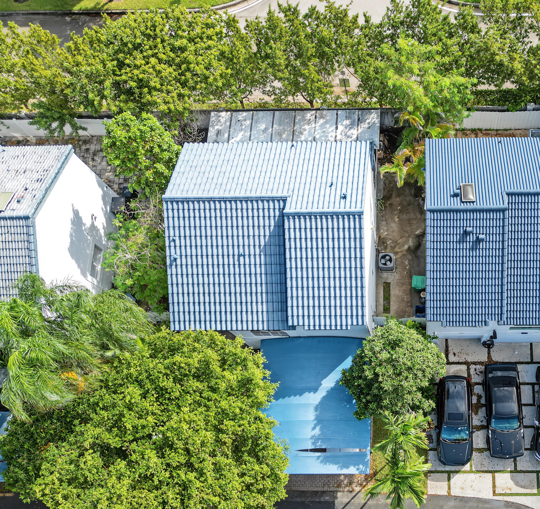 Aerial view featuring a multi-pitched roof with blue tile roofing, a covered front entryway, and a paved driveway with integrated landscaping grid