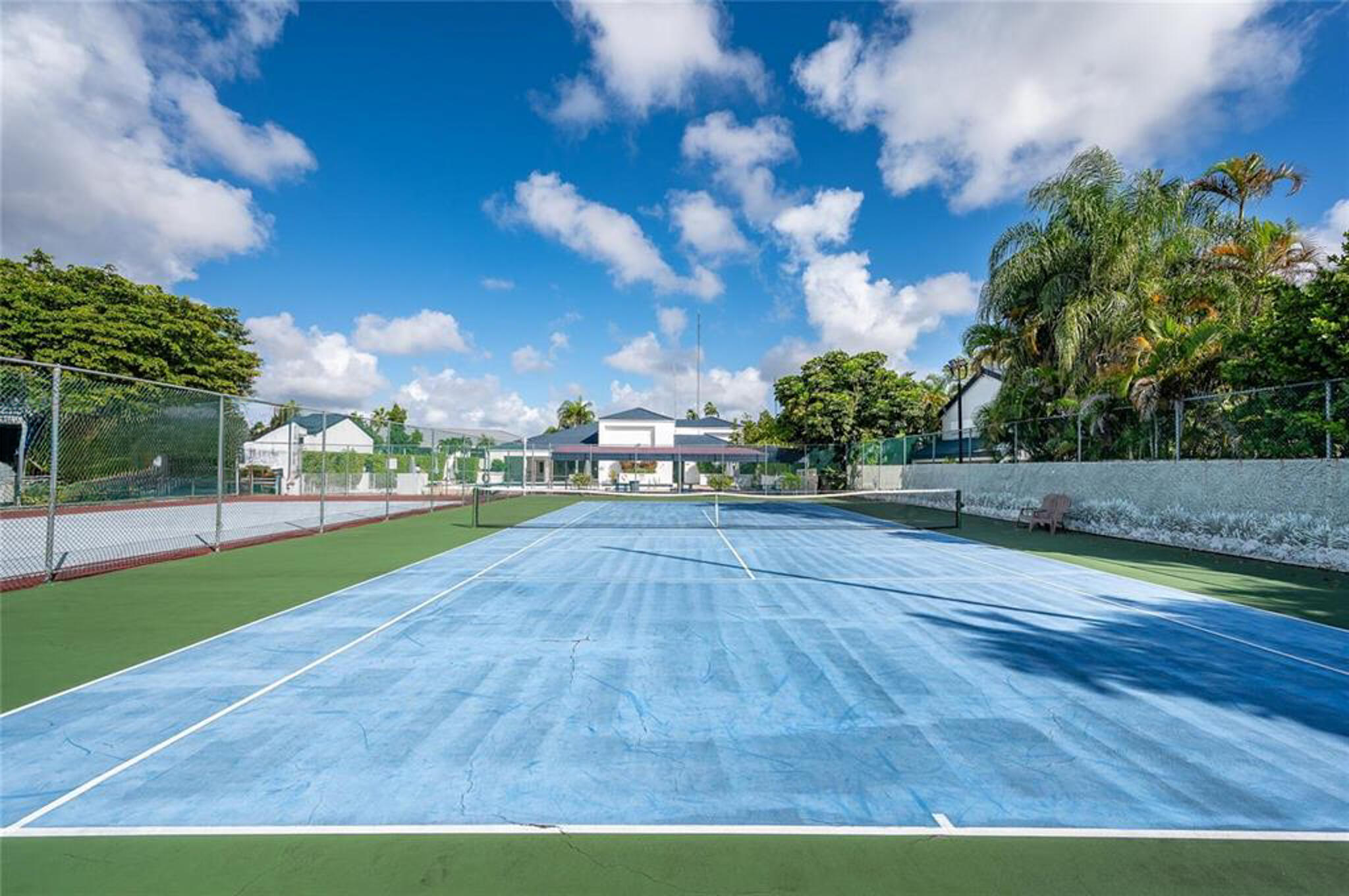 Dual-court outdoor tennis facility featuring painted hard surfaces, perimeter chain-link fencing, and mature landscaping