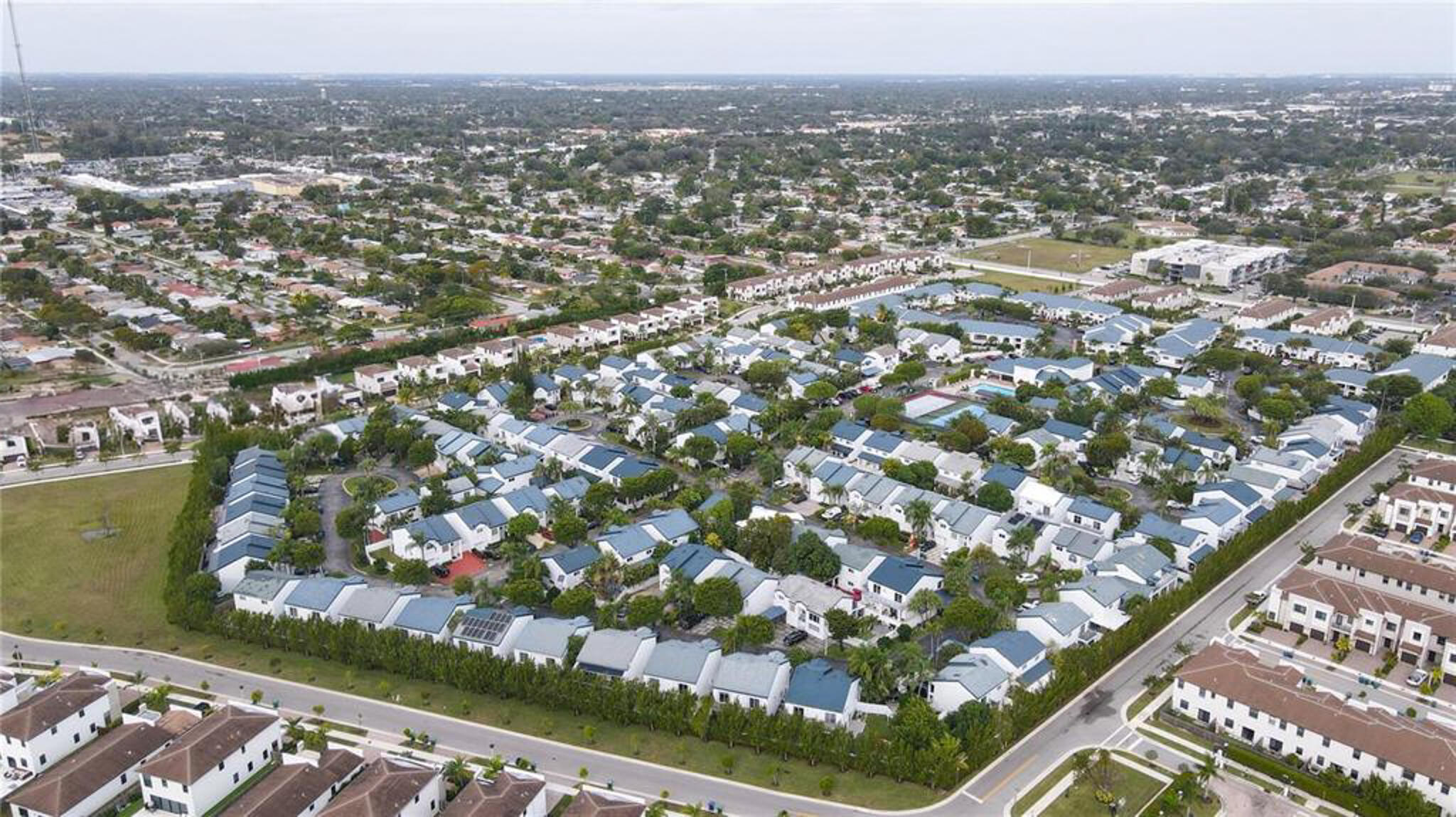 Aerial perspective of a planned community featuring multi-unit residential structures, uniform rooflines, paved access roads, and established mature landscaping