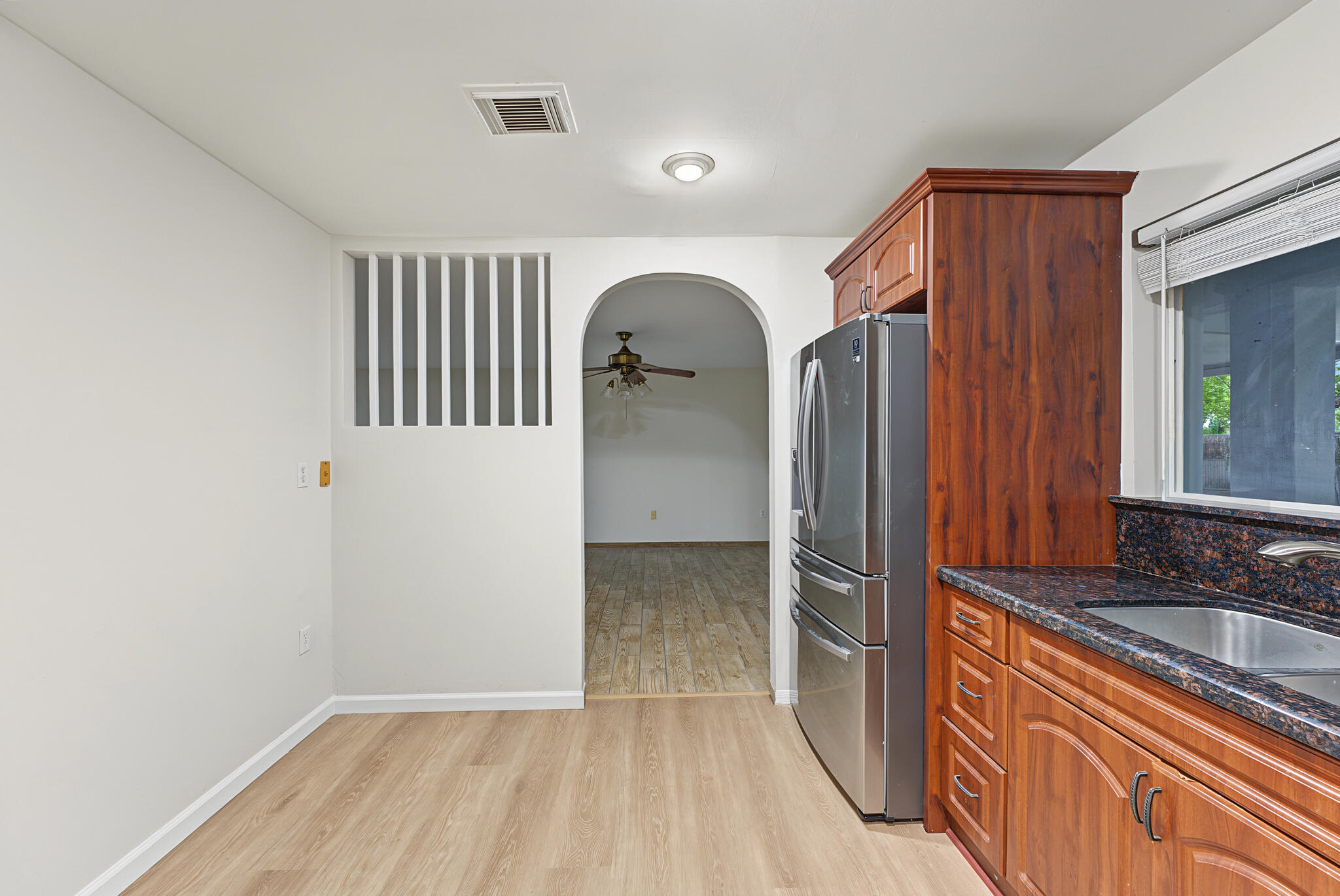 Kitchen featuring wood-finish cabinetry, stainless steel refrigerator, dark stone-style countertops, wood-finish flooring, and an arched entry