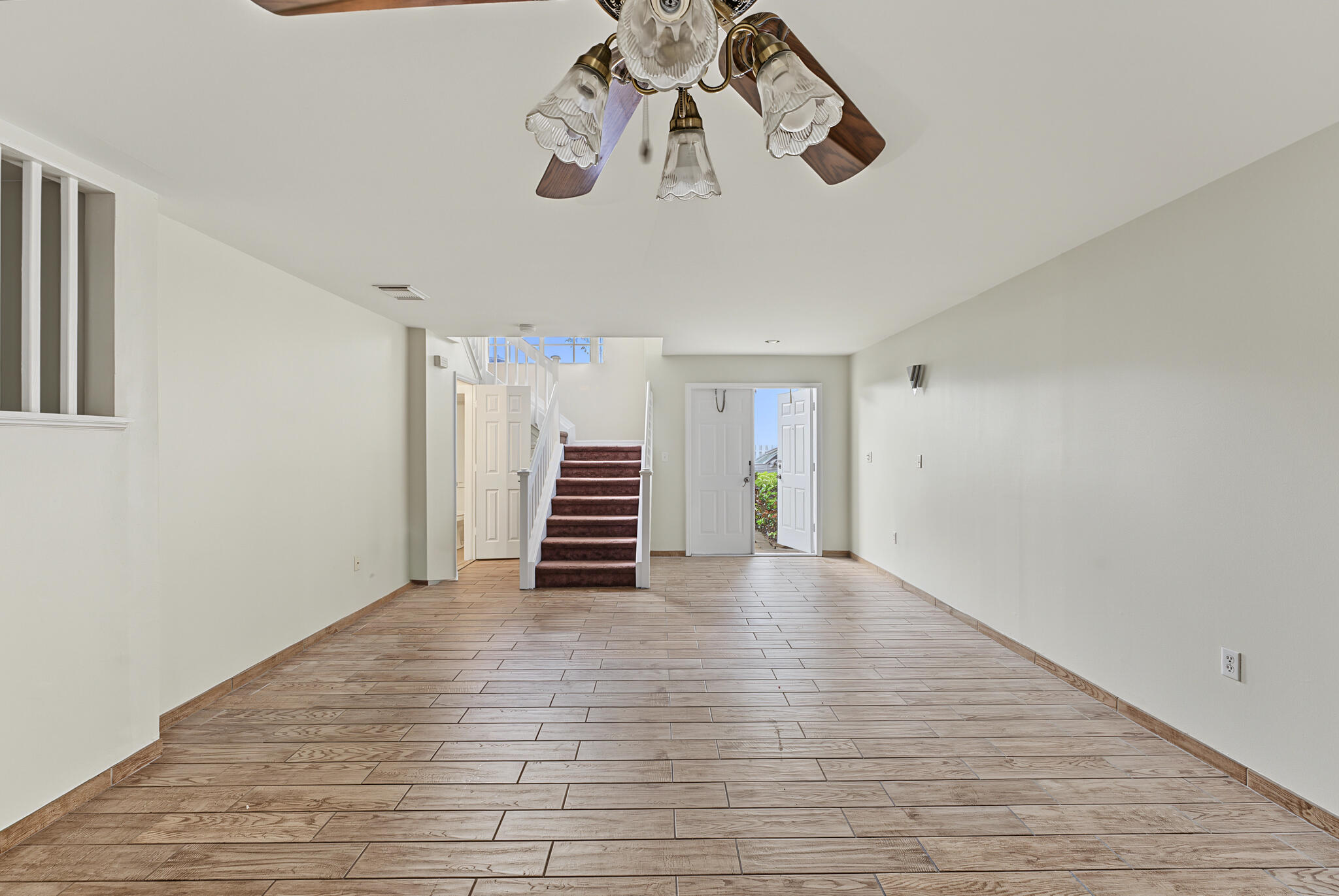 Open-concept interior featuring wood-finish tile flooring, a ceiling fan with multi-light fixture, and staircase with a carpeted runner