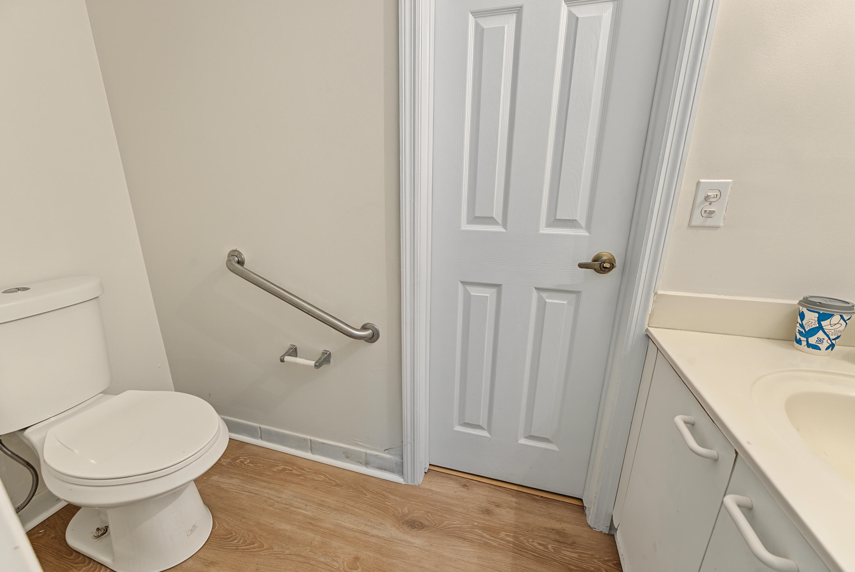 Bathroom featuring wood-finish flooring, a vanity with a solid-surface countertop, an integrated sink, and a wall-mounted stainless steel support rail