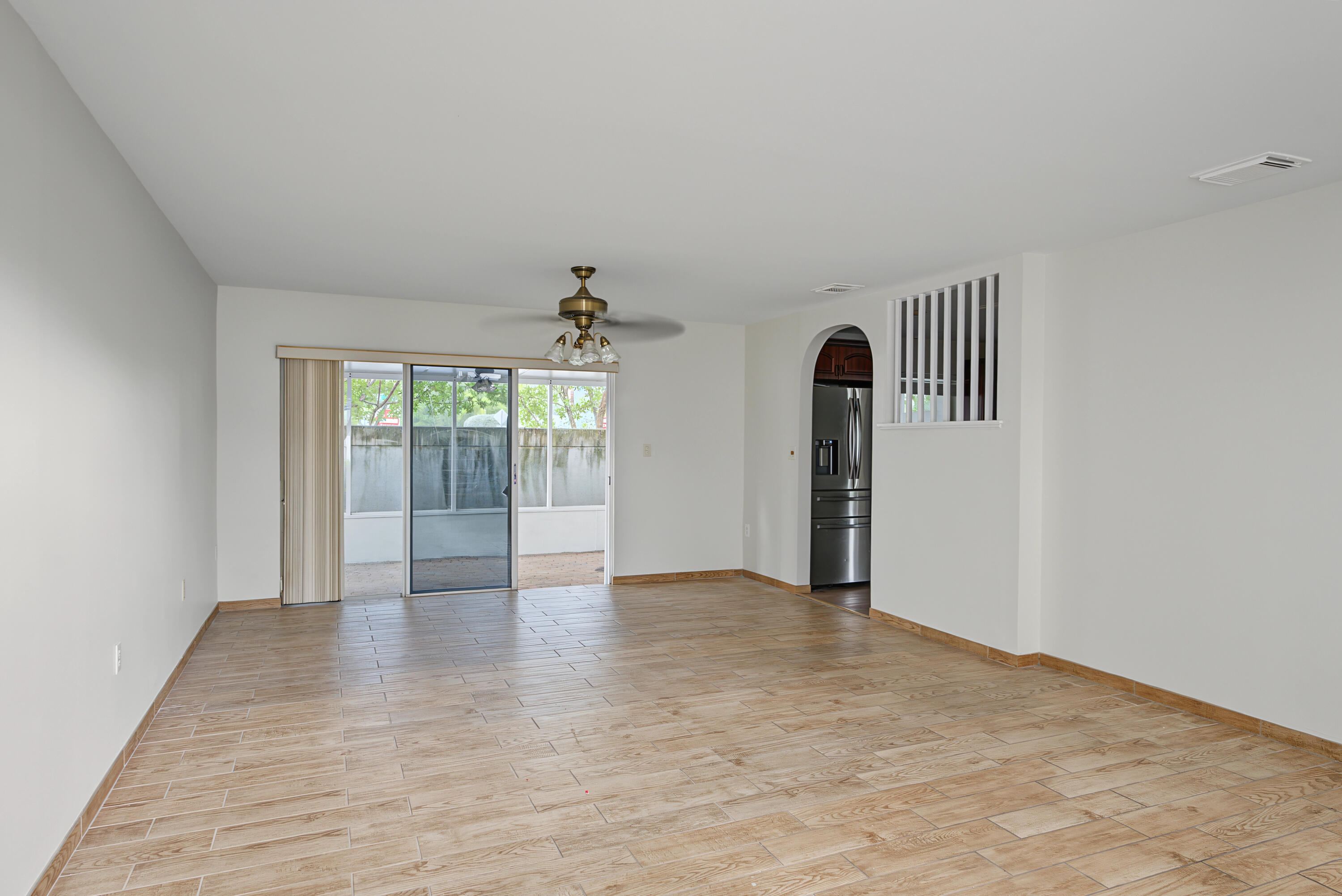 Neutral interior featuring wood-finish tile flooring, ceiling fan with integrated lighting, sliding glass door, arched doorway, and decorative spindle partition
