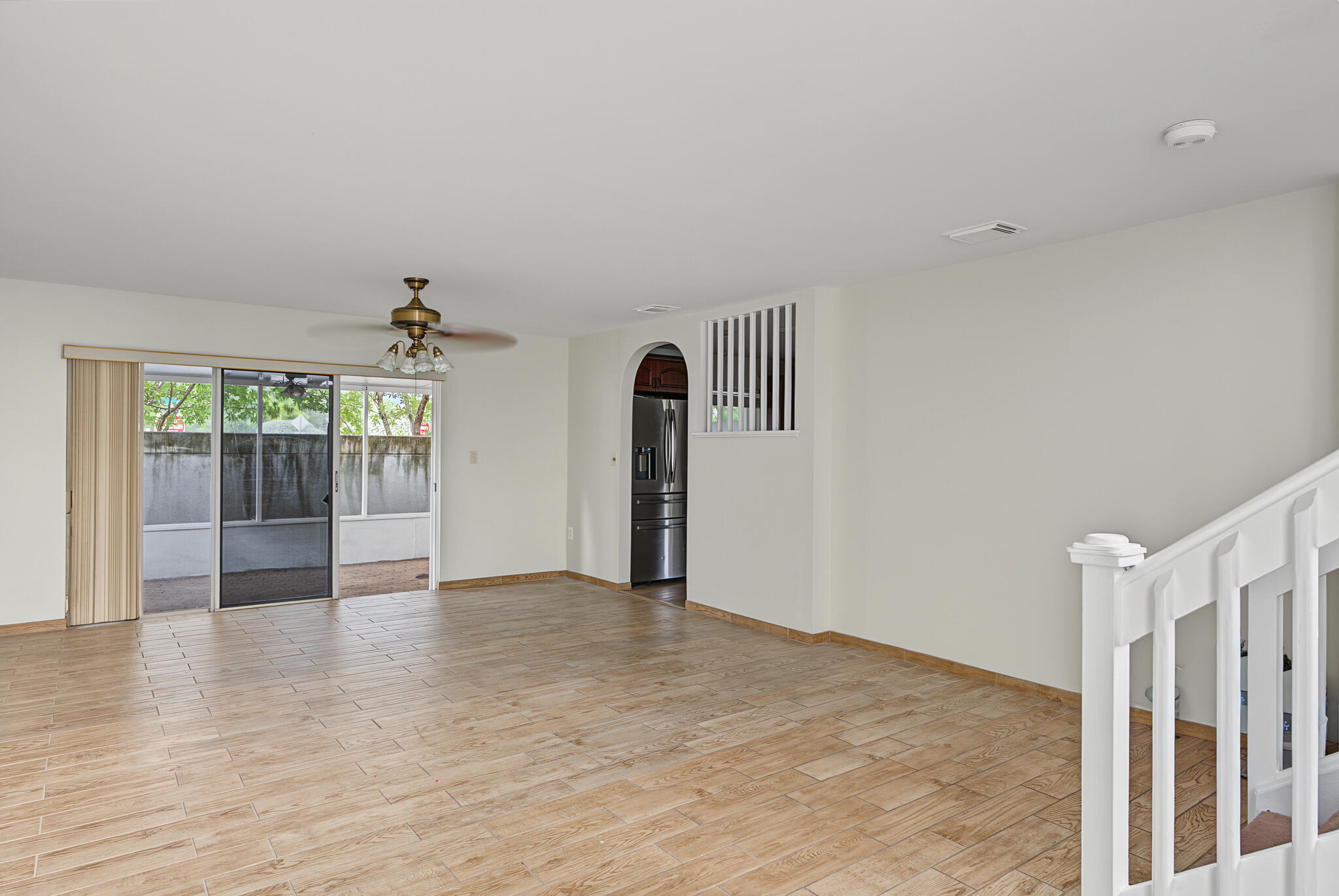 Open interior space featuring wood-finish flooring, a ceiling fan with integrated lighting, a sliding glass door, an arched entryway, and a white balustrade staircase