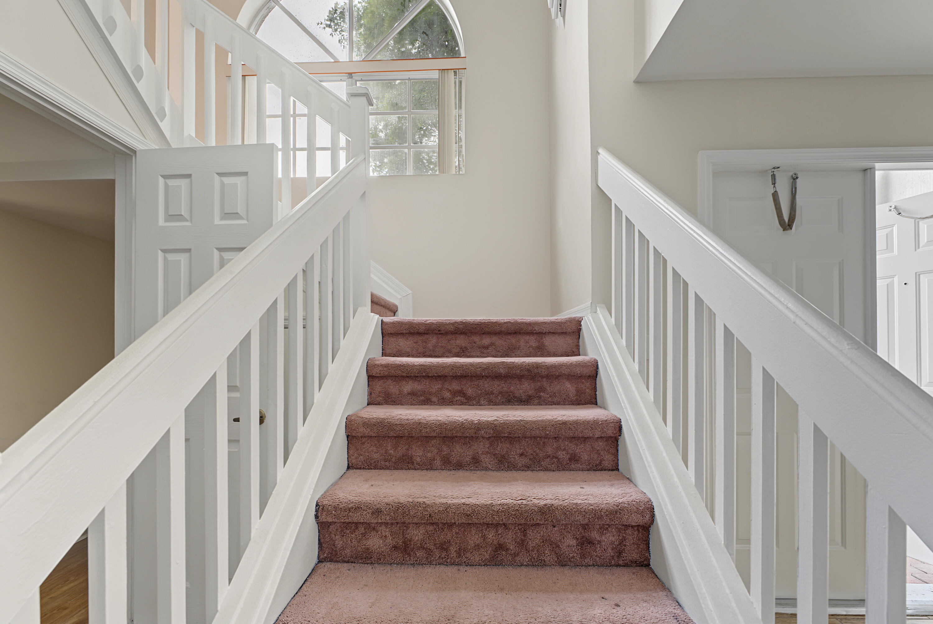 Staircase featuring white balusters and handrails with an arched window