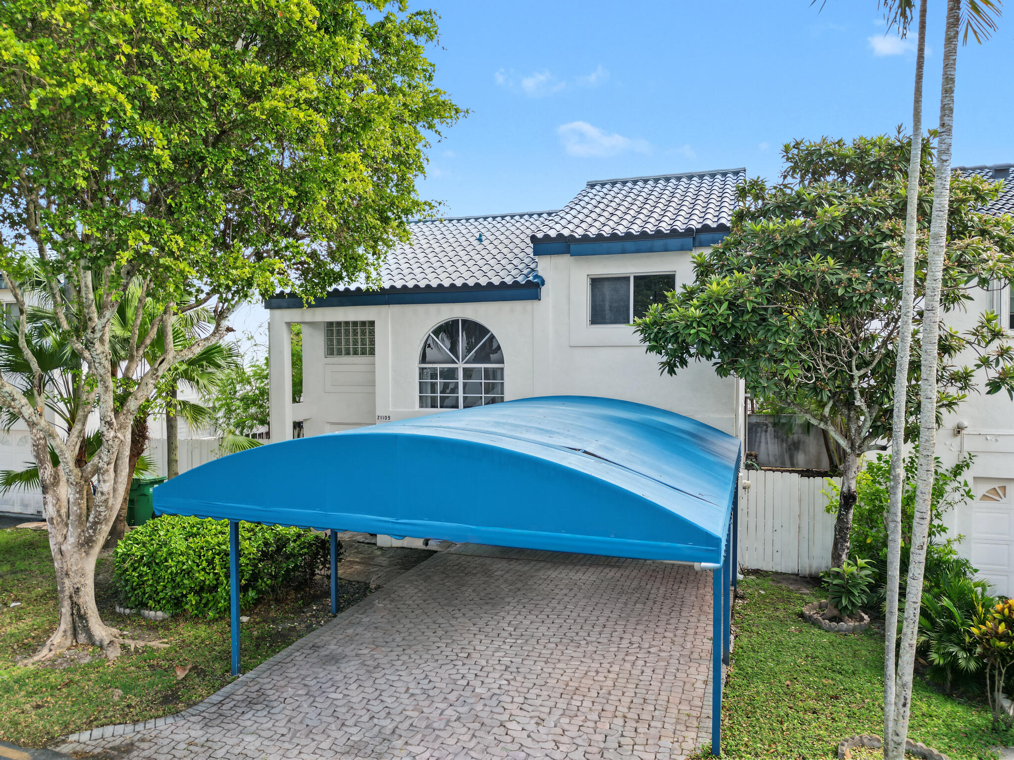 Stucco exterior featuring a tiled roof, arched window, and paved driveway with a covered carport Stucco exterior featuring a tiled roof, arched window, and paved driveway with a covered carport