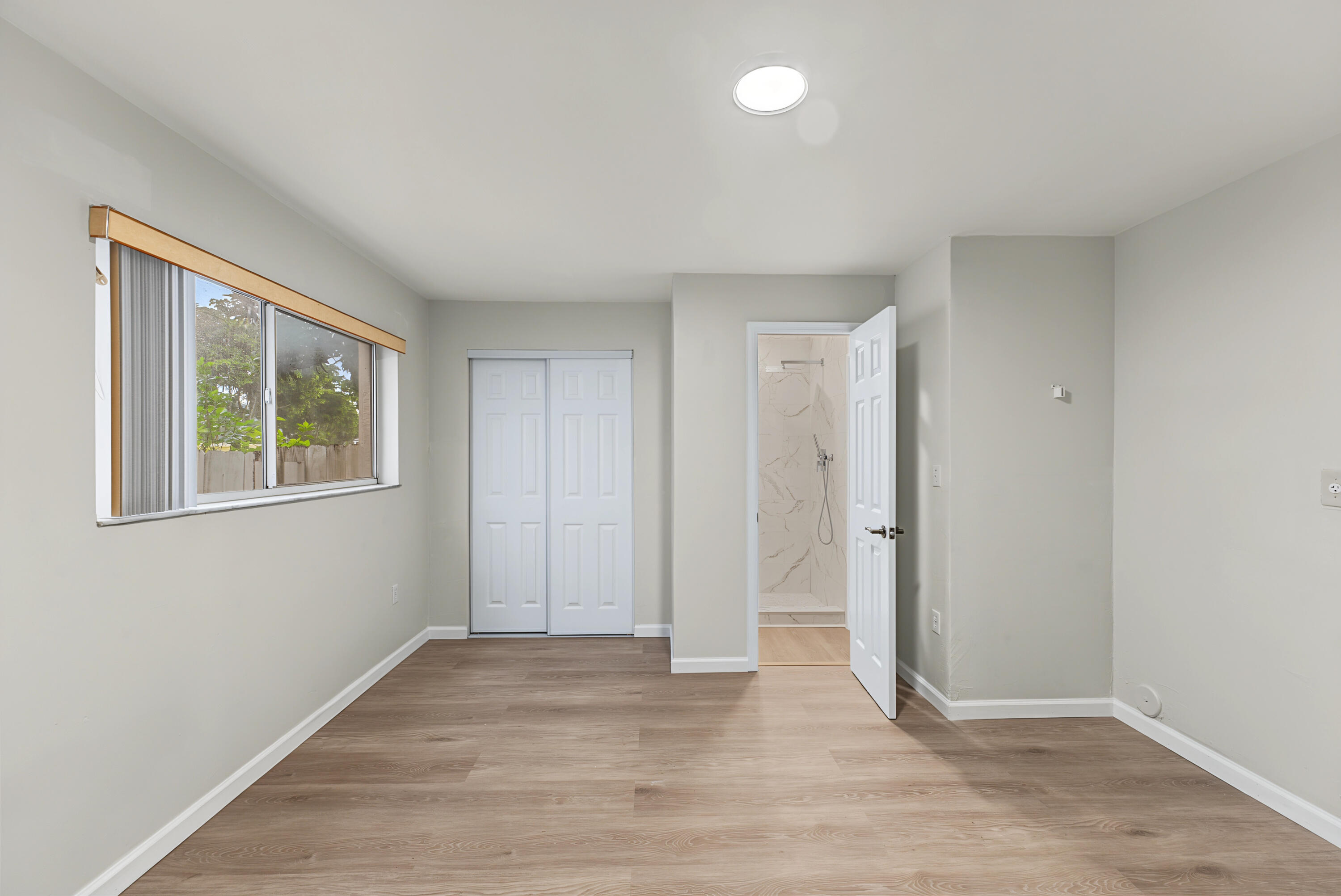 Neutral-toned interior featuring wood-finish flooring, a horizontal sliding window, dual-paneled closet doors, and recessed ceiling lighting
