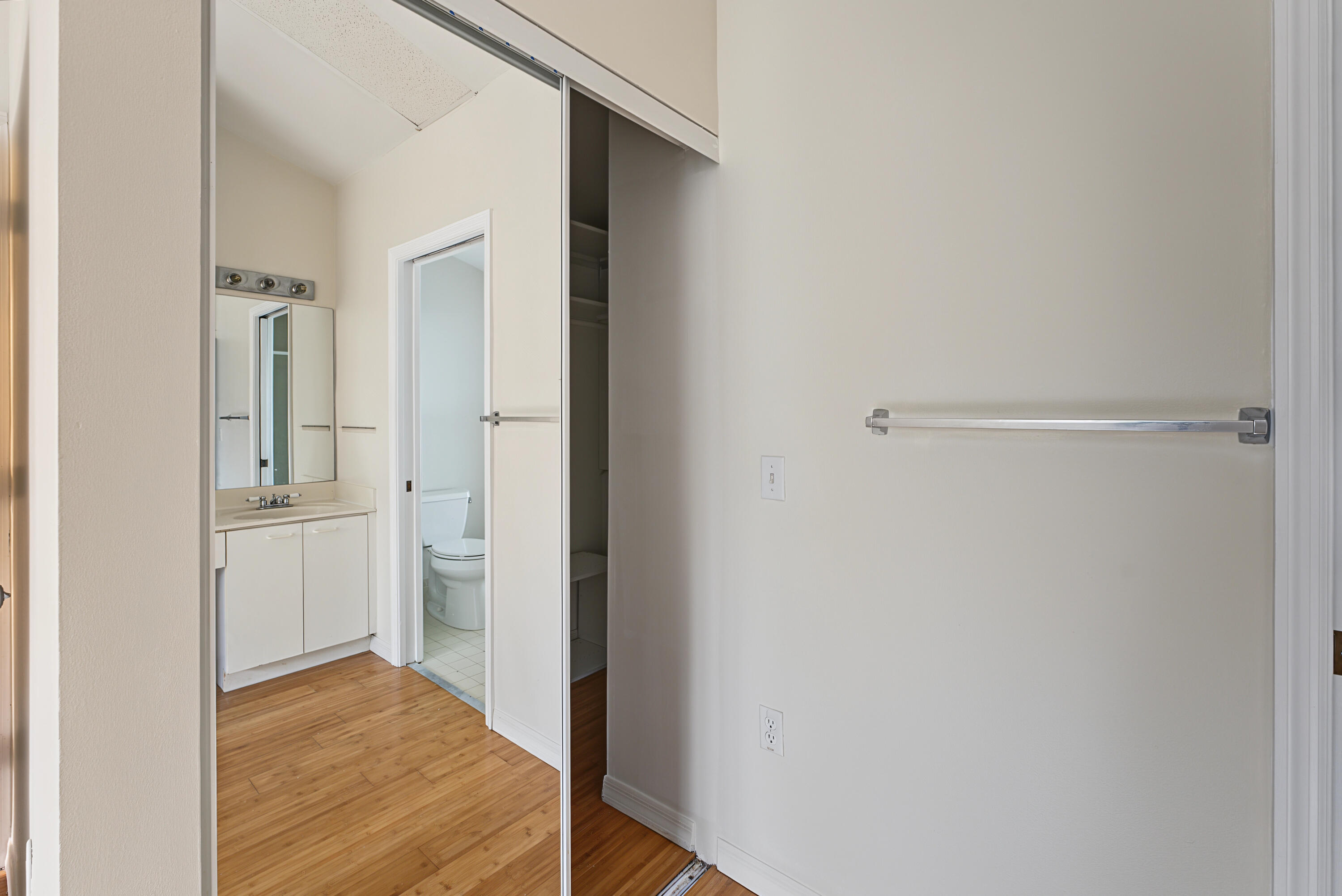 Sliding mirrored closet doors, wood-finish flooring, white vanity with countertop sink, and wall-mounted metal towel rack