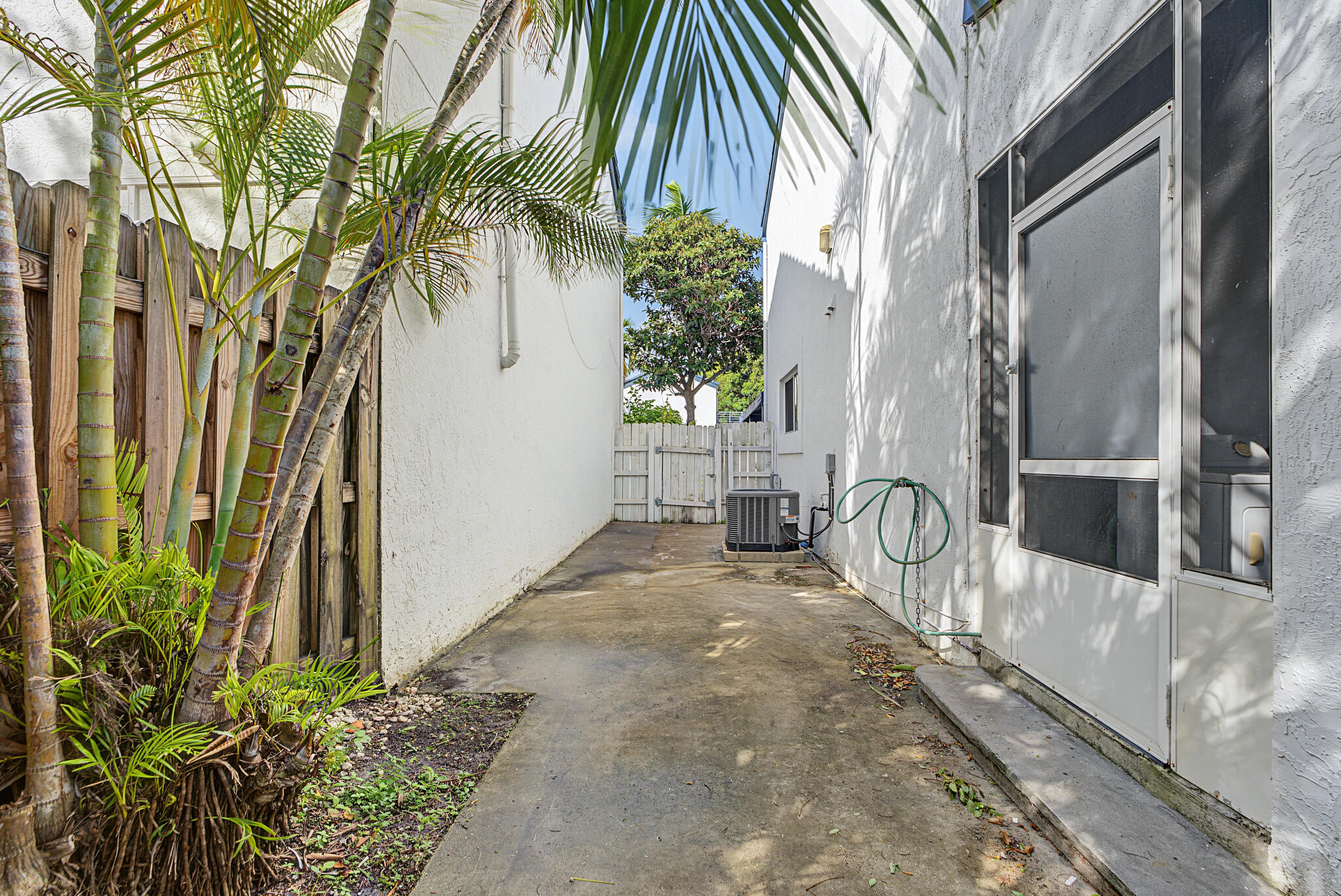 Exterior side yard featuring a concrete pathway, white wood-slat privacy fencing, stucco exterior walls, and a screened entry door