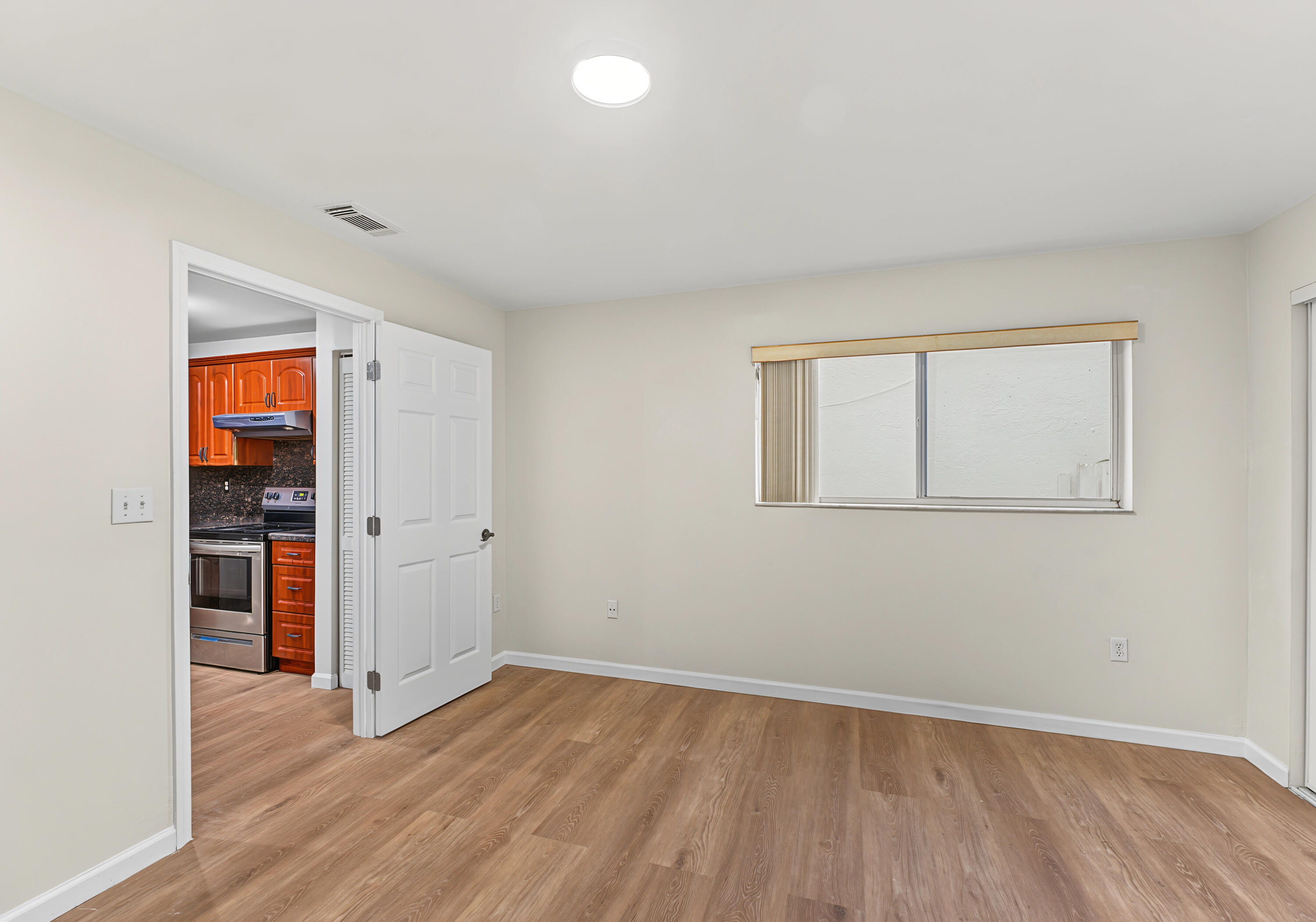 Neutral-toned interior space featuring wood-finish flooring, a recessed ceiling light, a sliding window with vertical blinds, and a white six-panel door